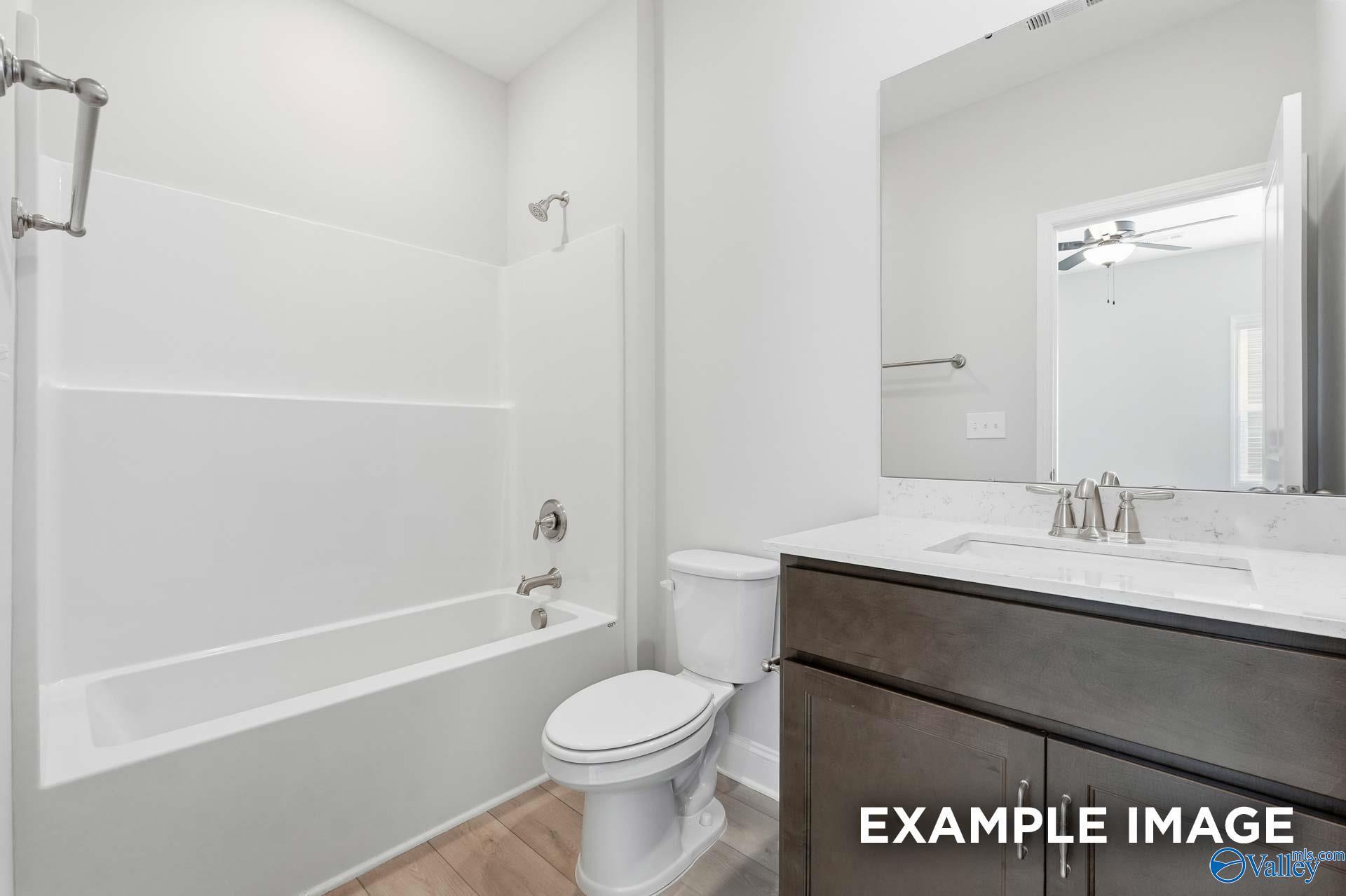 Bright bathroom with white tub-shower combo, dark wood vanity, quartz sink in Davidson Homes The Harrison C, Madison, Alabama