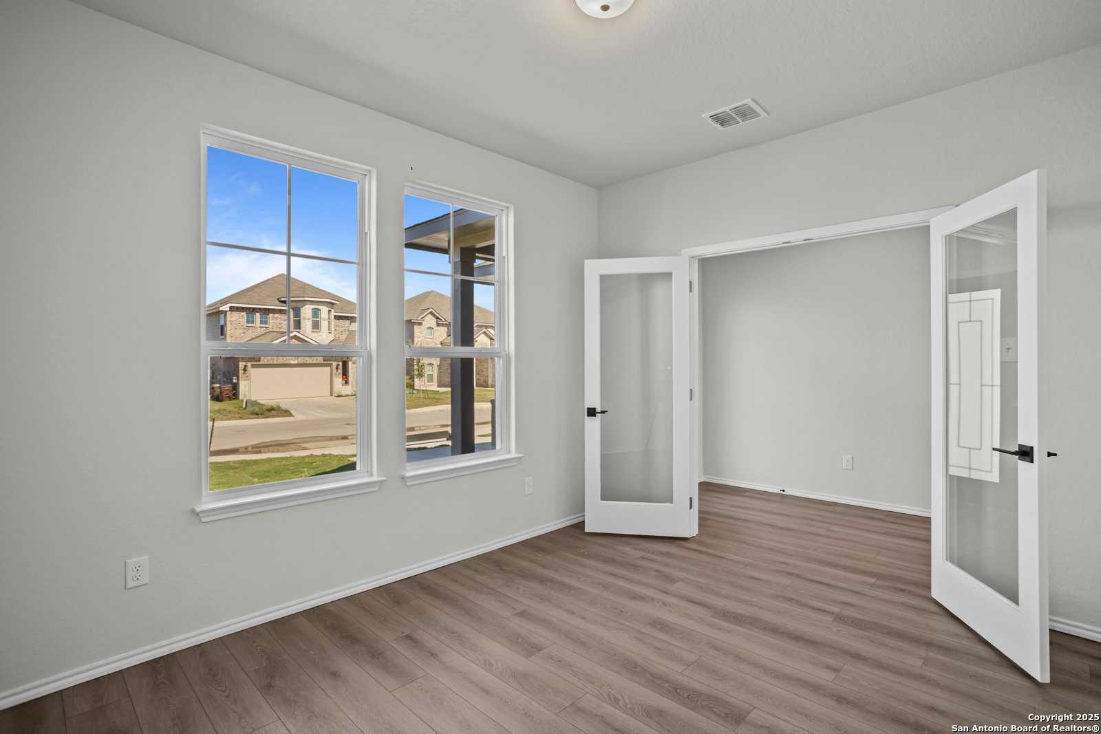 Bright living room with hardwood floors, large windows, and open French doors to covered patio in Davidson Homes The Douglas B, Converse, Texas