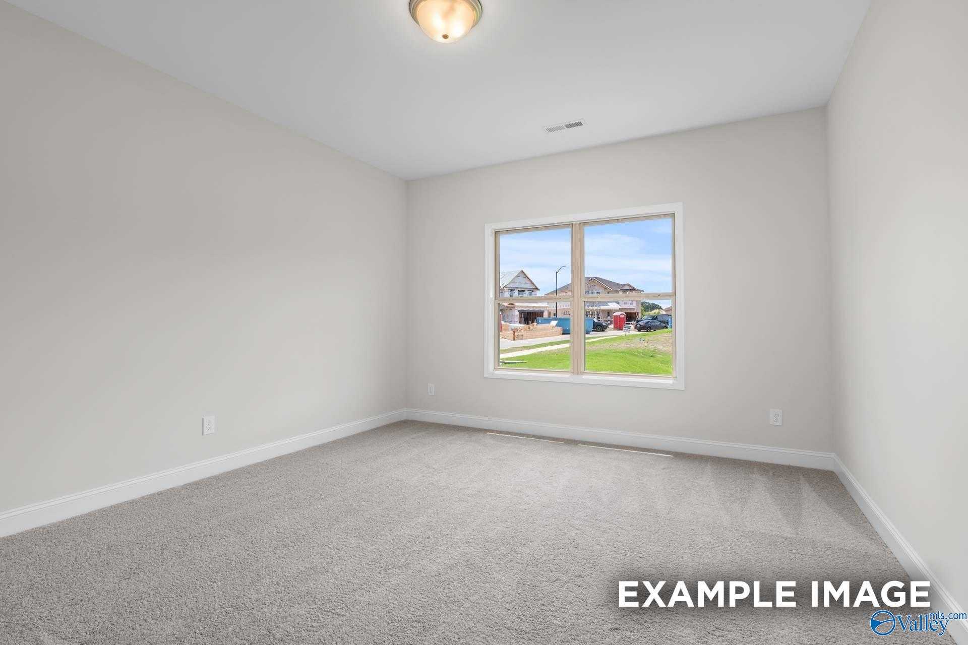Bright empty bedroom with neutral walls, carpet flooring, and large window view of neighborhood in The Daphne D, Arab, Alabama
