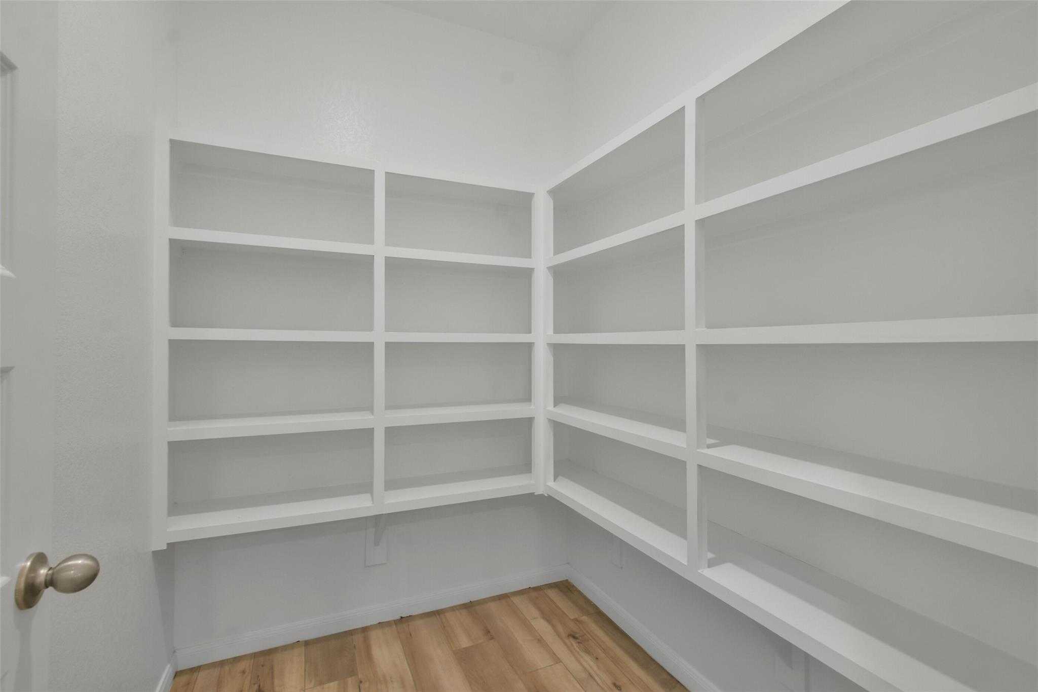Spacious walk-in closet with white built-in shelves and hardwood floors in Davidson Homes The Tierra A, Dayton, Texas