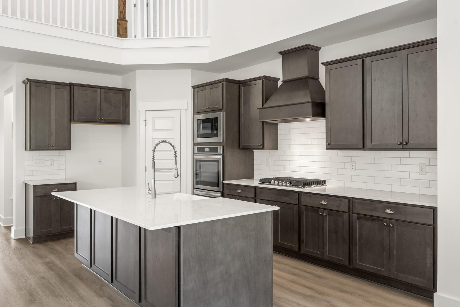 Modern kitchen with dark cabinets, quartz island, and stainless appliances in The Ridgeport C at Woods Crossing, Gallatin.