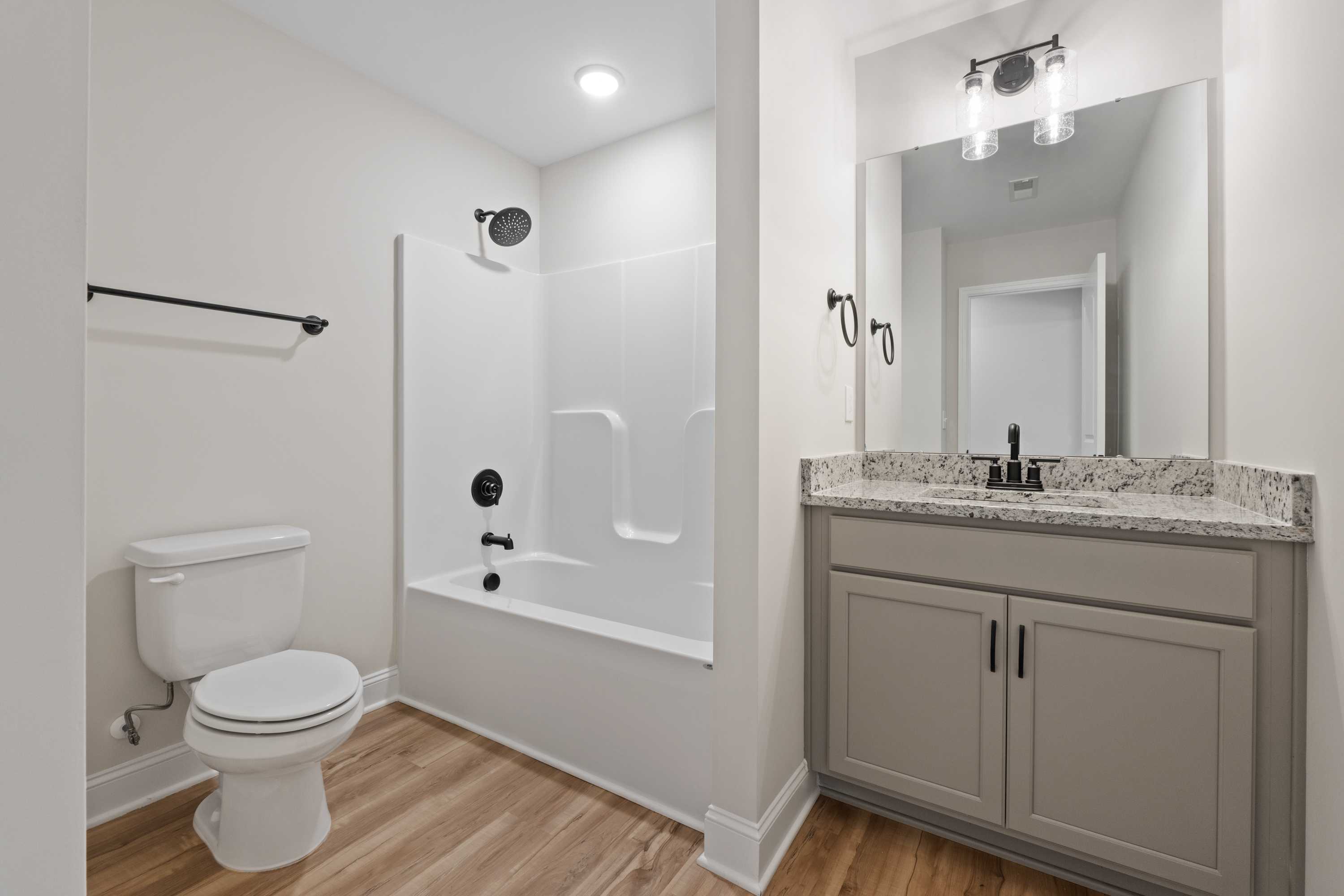 Spacious guest bathroom in The Everett C with white tub-shower combo, gray shaker vanity, quartz counters, and hardwood floors