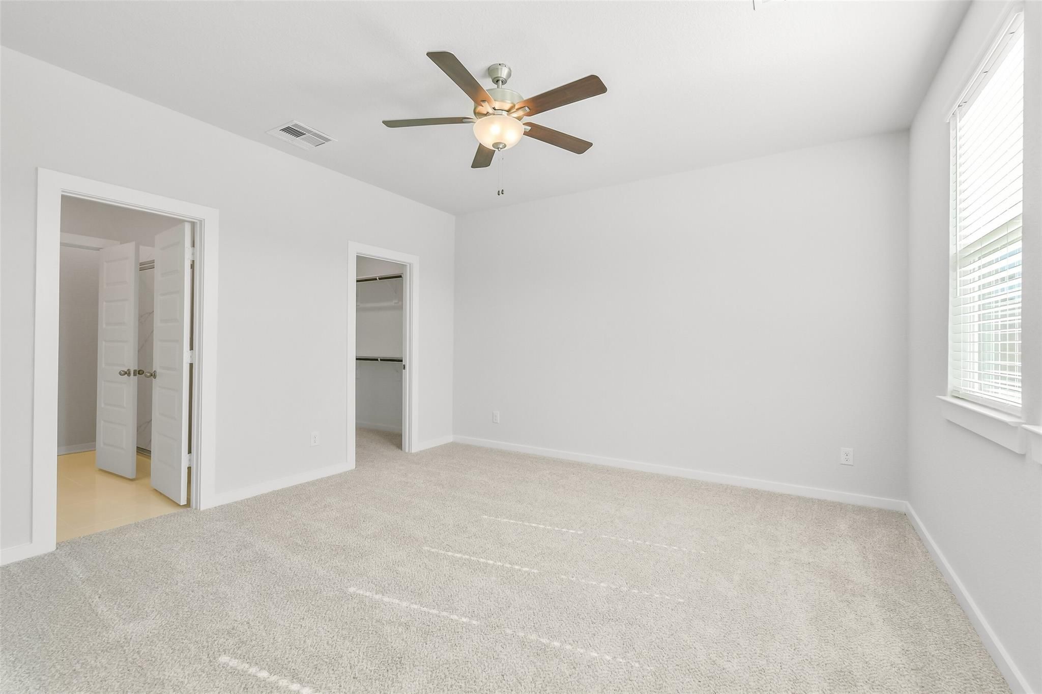 Spacious secondary bedroom with ceiling fan, beige carpet, walk-in closet, and en-suite door in Davidson Homes San Marcos E, Cleveland, Texas