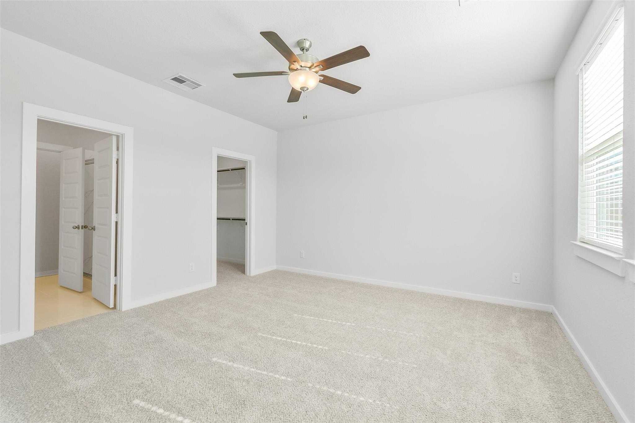 Spacious secondary bedroom with ceiling fan, beige carpet, walk-in closet, and en-suite door in Davidson Homes San Marcos E, Cleveland, Texas