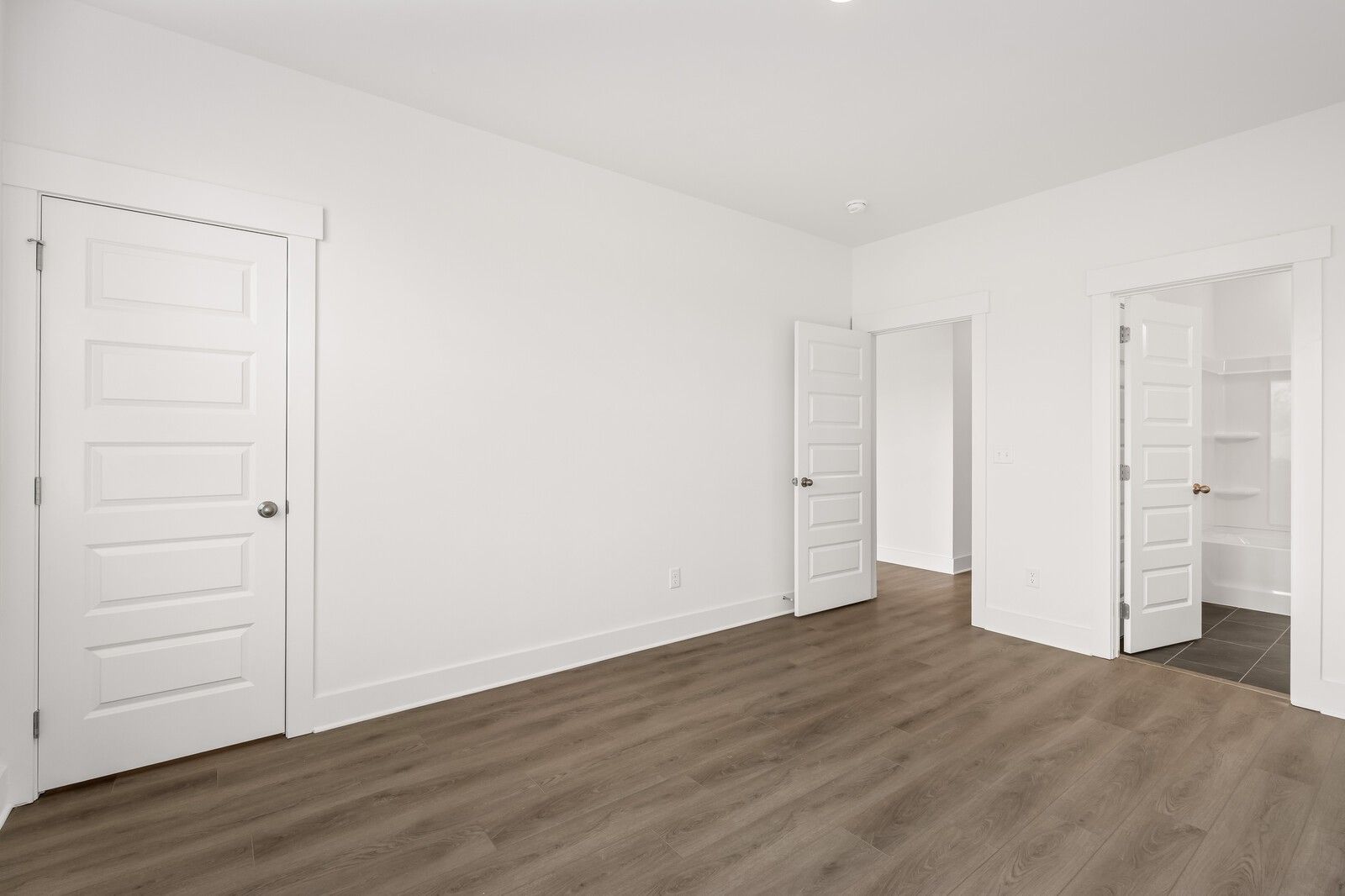 Bright secondary bedroom with white paneled doors, open closets, and hardwood floors in Davidson Homes The Willow D, Mt. Juliet