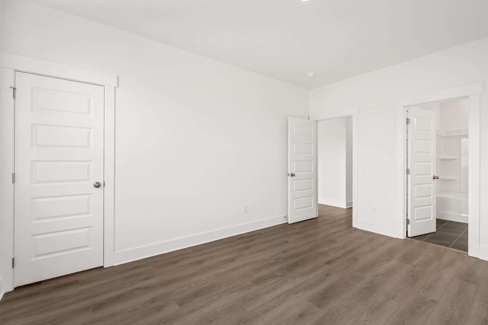 Bright secondary bedroom with white paneled doors, open closets, and hardwood floors in Davidson Homes The Willow D, Mt. Juliet