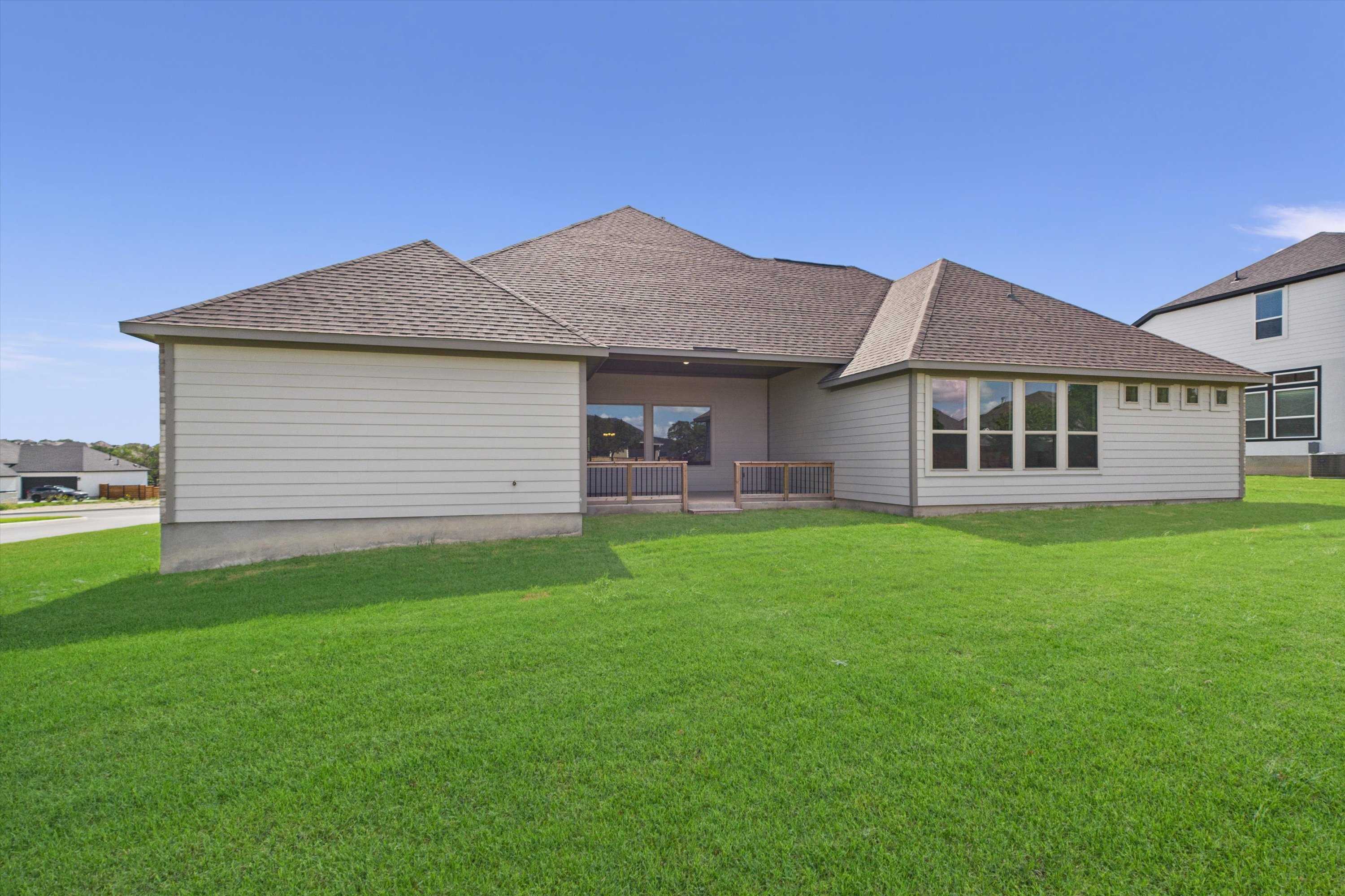 Back view of single-story 4-bedroom home with covered patio, large windows, and lush green yard in Potranco Oaks, Castroville, Texas