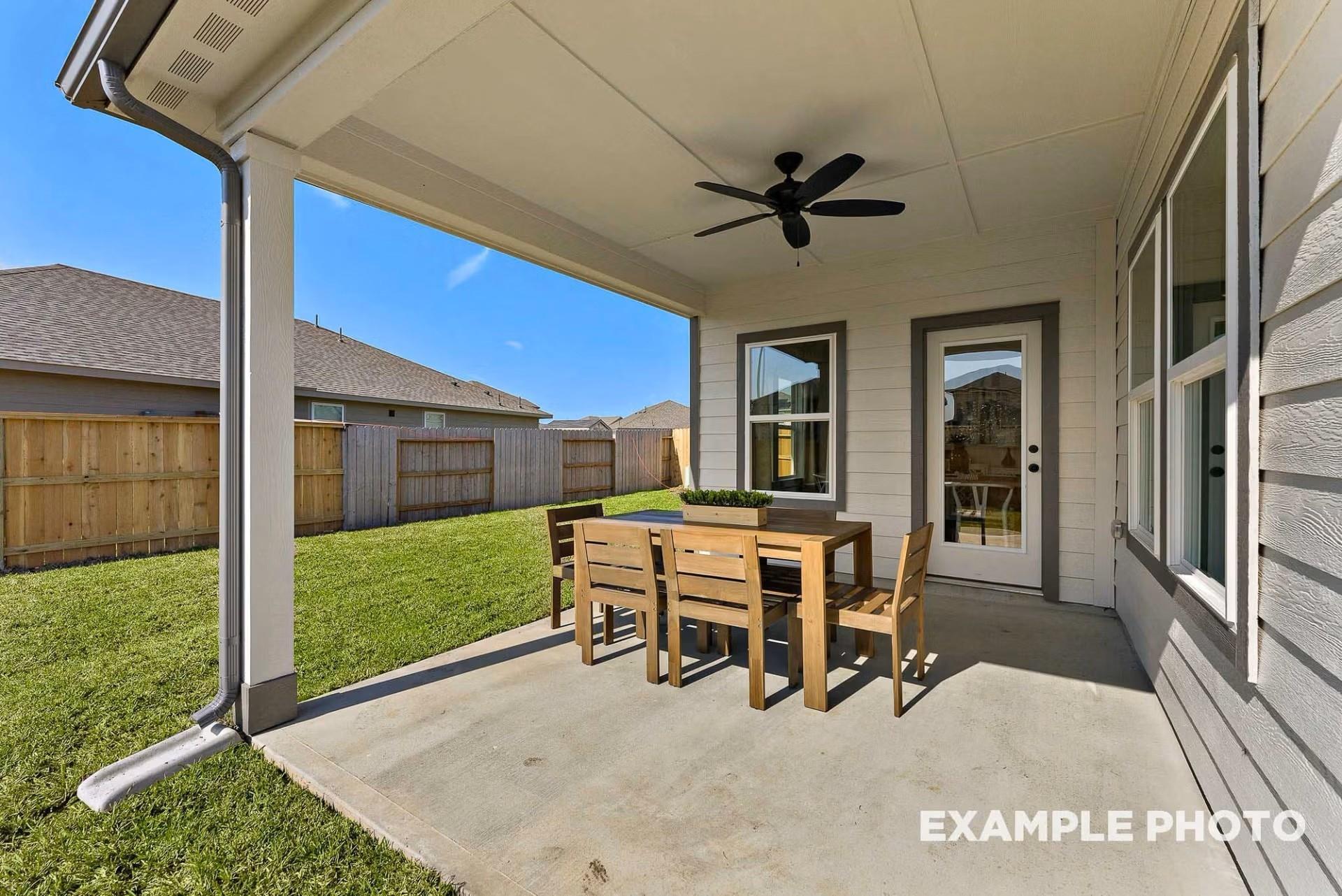 Covered back patio with wooden dining table, ceiling fan, and green lawn in Davidson Homes The Everett C, River Ranch Meadows, Dayton, Texas