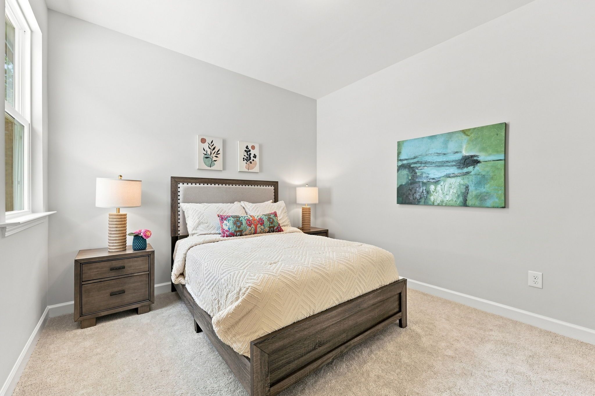 Cozy secondary bedroom in The Jordan A featuring a modern wood bed frame, neutral bedding, and vibrant wall art.