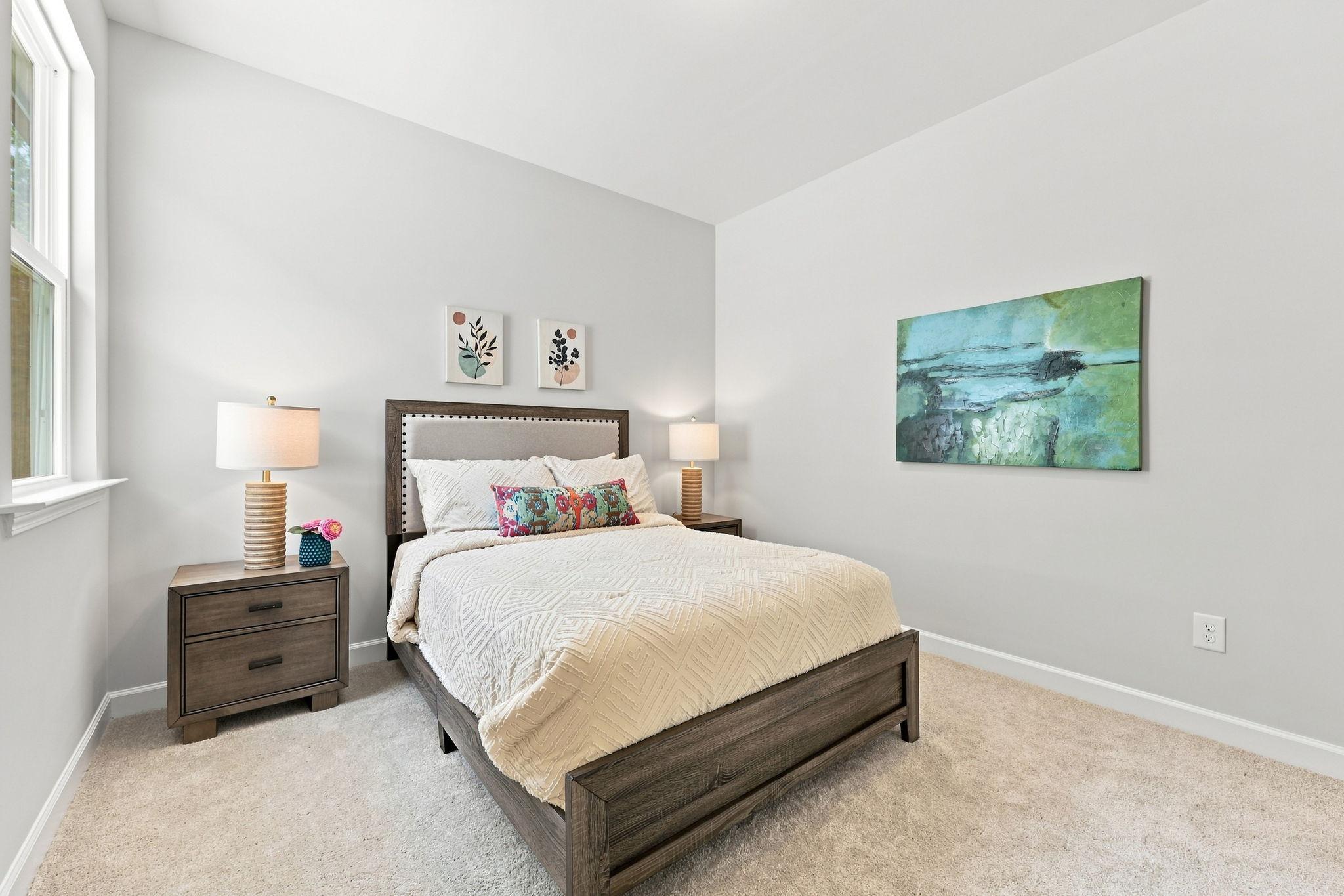 Cozy secondary bedroom in The Jordan A featuring a modern wood bed frame, neutral bedding, and vibrant wall art.