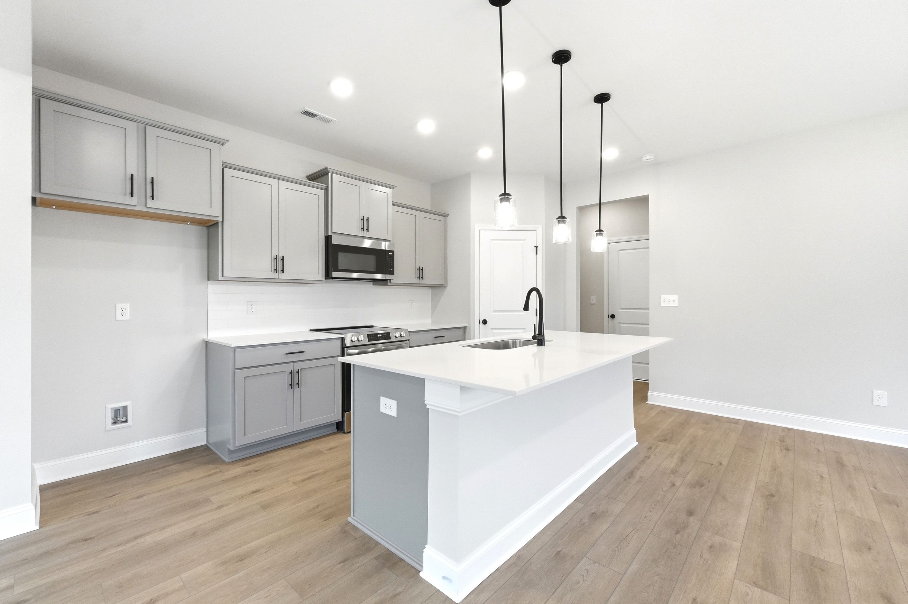 Modern kitchen in The Russell by Davidson Homes featuring grey cabinets, quartz countertops, and a central island.