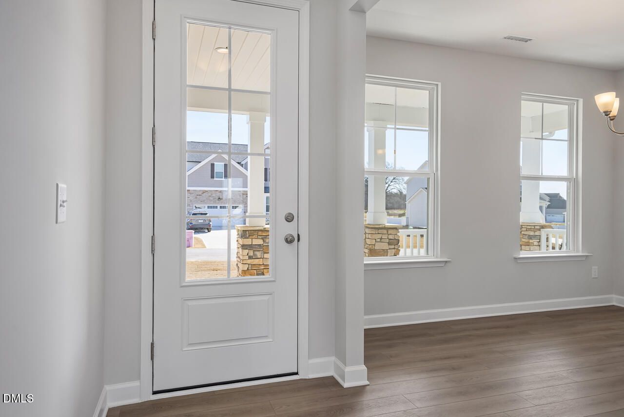 Bright front entryway with open white door revealing covered porch and stone pillars, gray walls, luxury vinyl plank floors in Davidson Homes Willow G, Angier NC