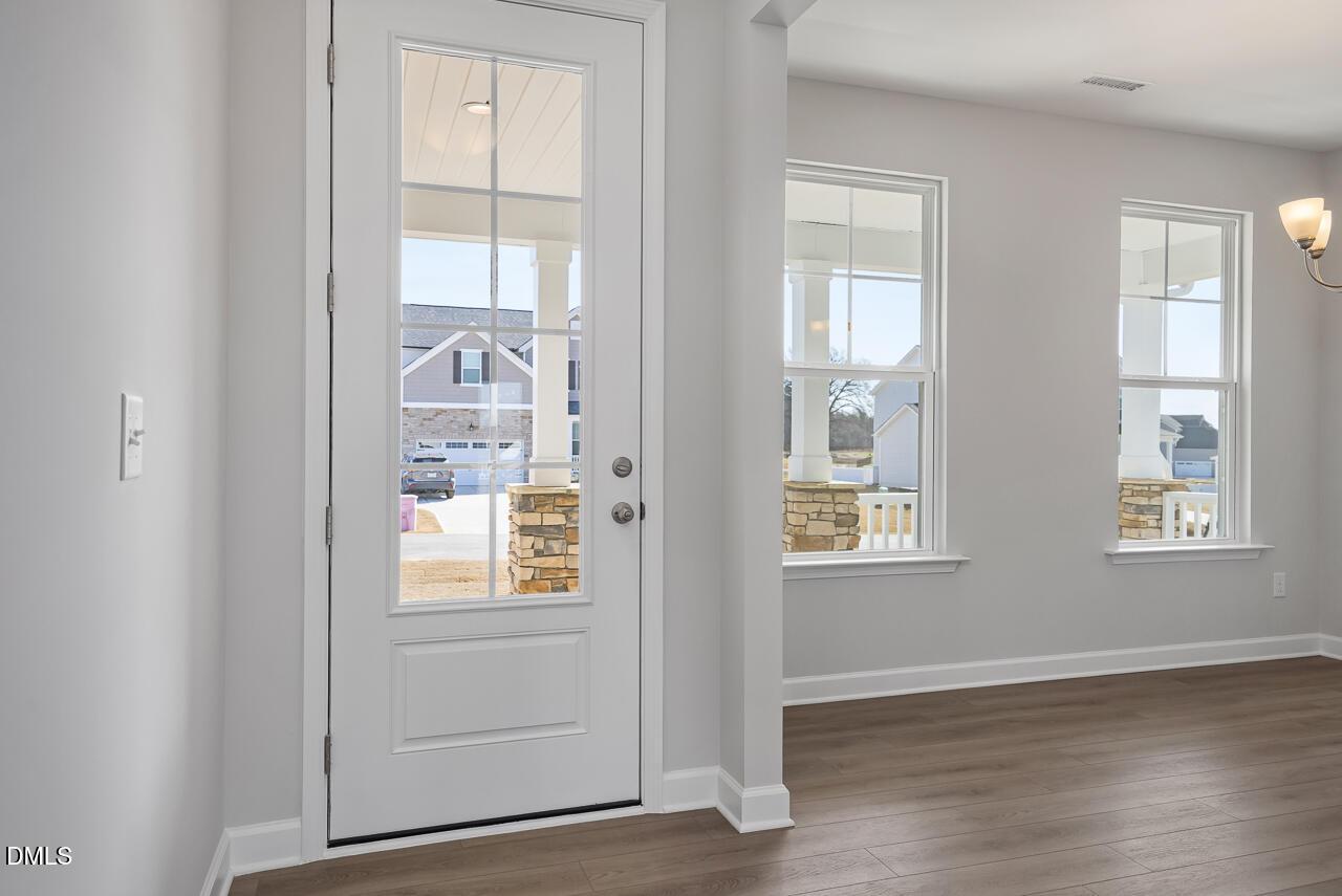 Bright front entryway with open white door revealing covered porch and stone pillars, gray walls, luxury vinyl plank floors in Davidson Homes Willow G, Angier NC