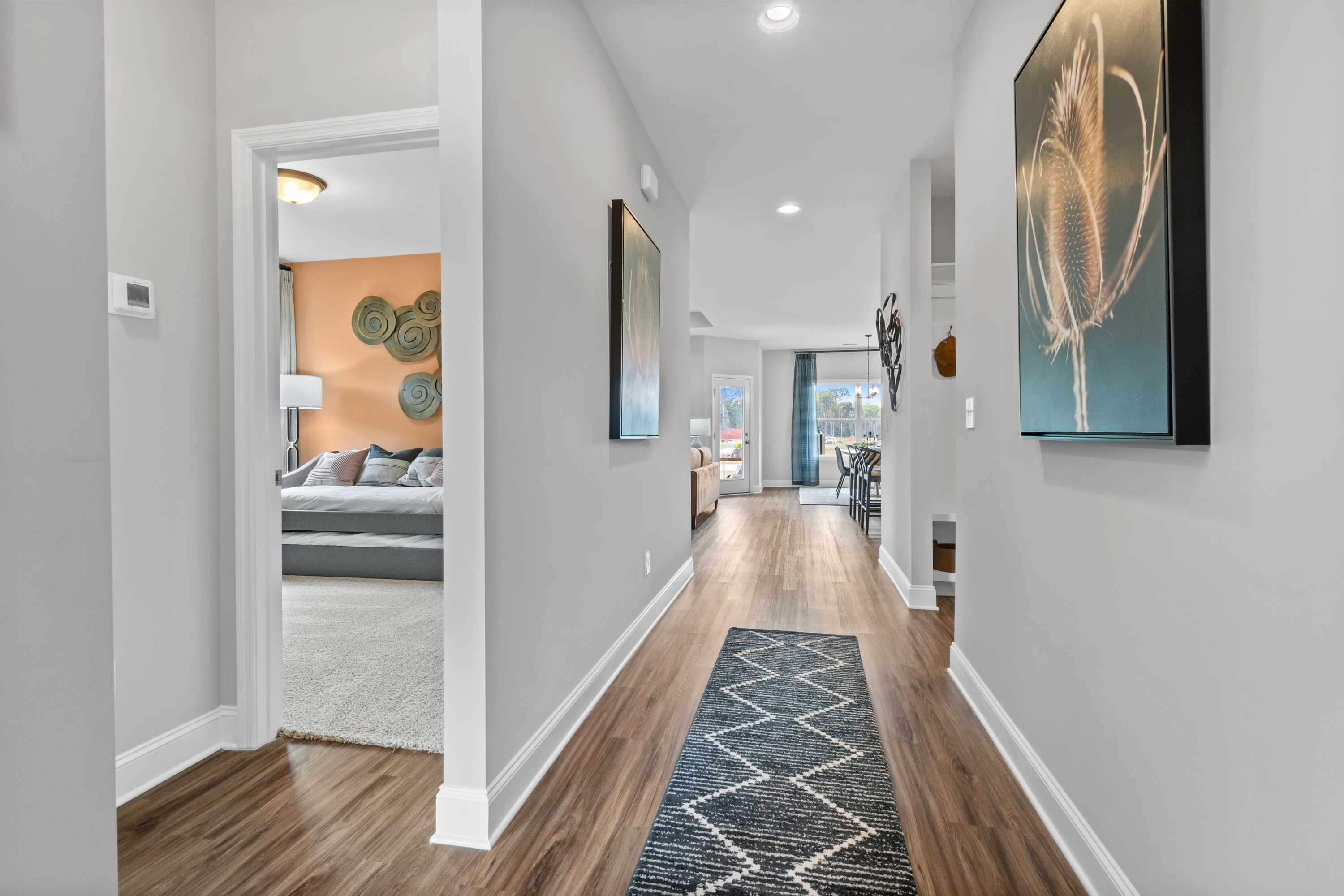 Spacious hallway with hardwood floors, gray walls, blue runner rug, and wall art in Wood Trail home, Toney Alabama