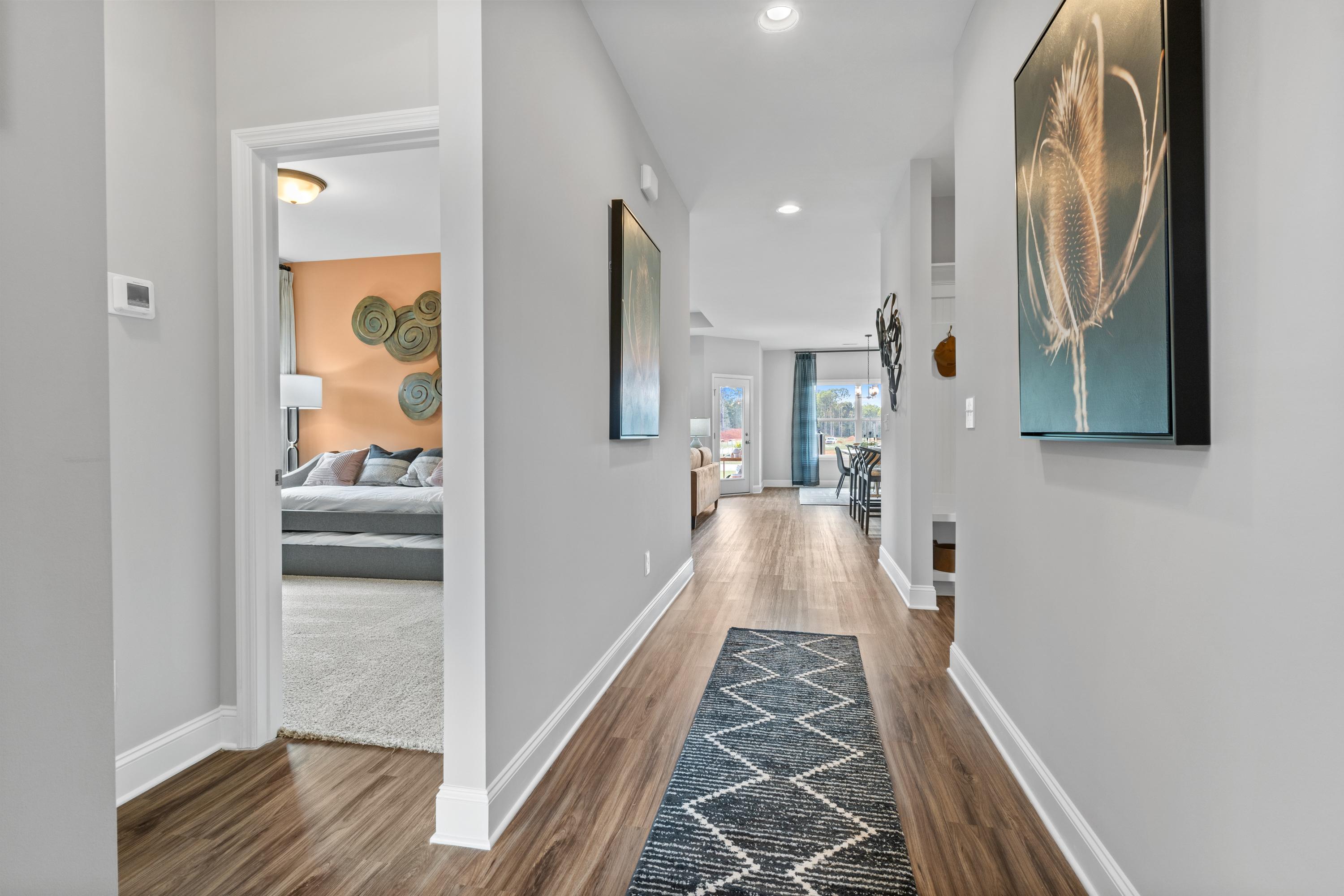 Spacious hallway with hardwood floors, gray walls, blue runner rug, and wall art in Wood Trail home, Toney Alabama