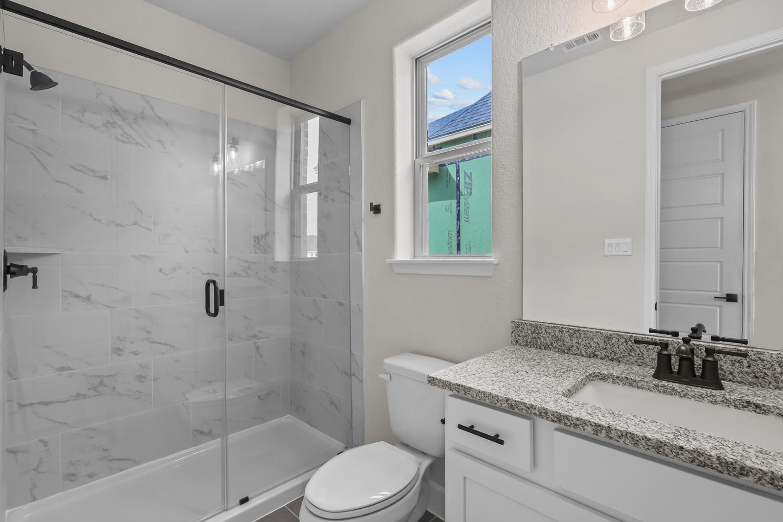 Modern bathroom in The Belmont featuring a walk-in glass shower with marble-look tile and granite vanity countertop.