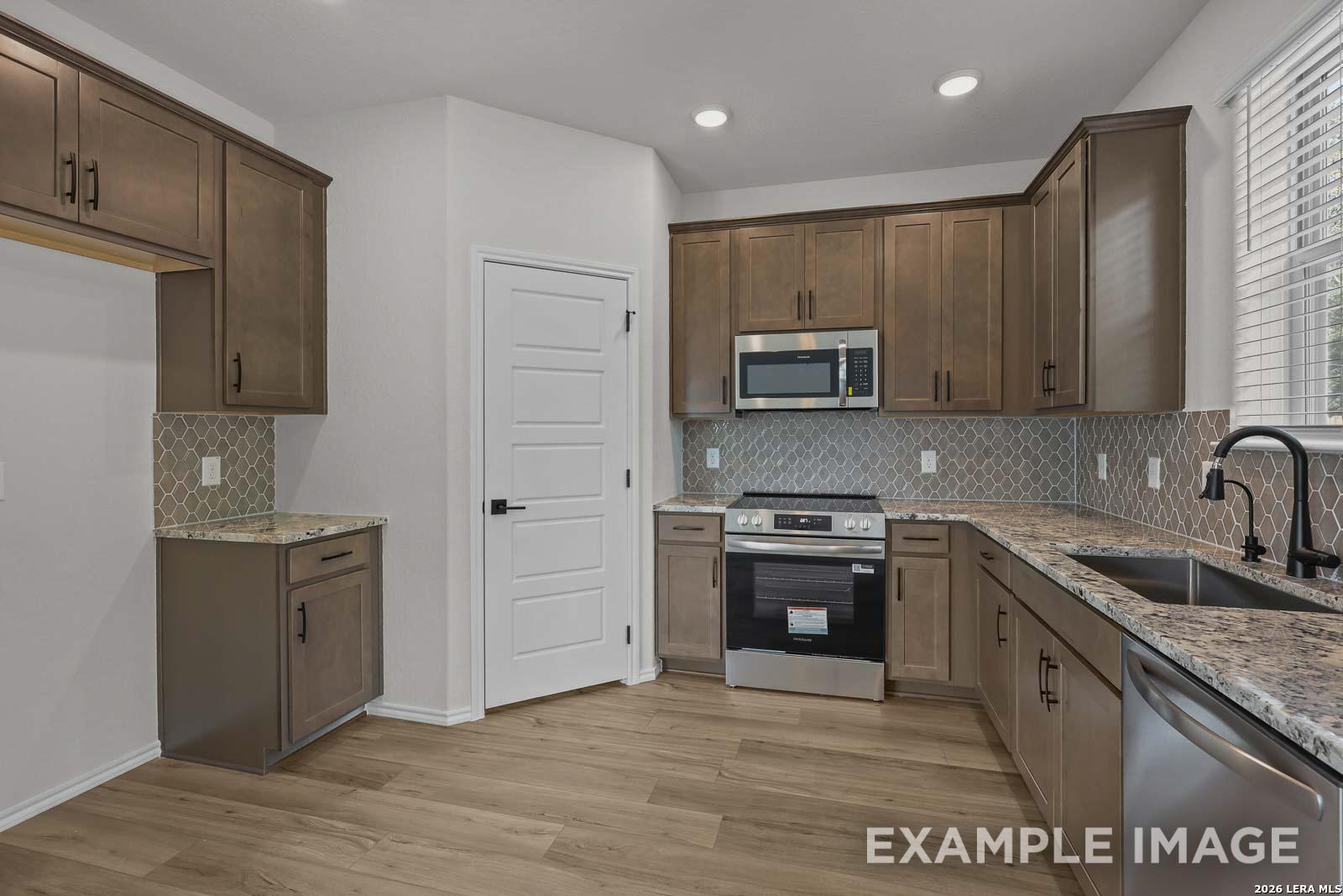 Modern kitchen with granite countertops, stainless appliances, and wood-style flooring in The Florence A, San Antonio, TX.