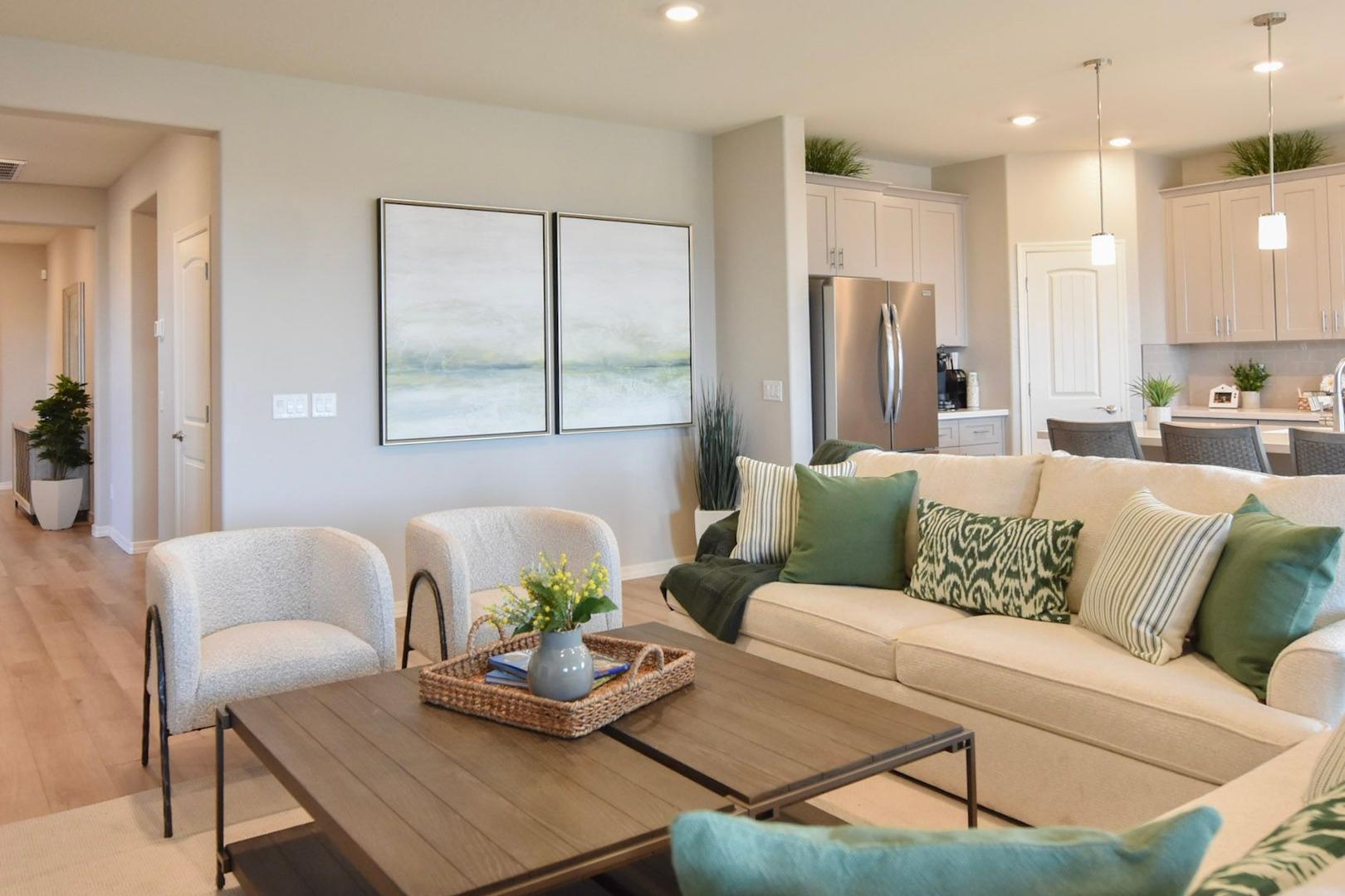Open-concept living room in The Harmony B Davidson Homes plan featuring white sofa, green pillows, wooden coffee table, and adjacent white kitchen