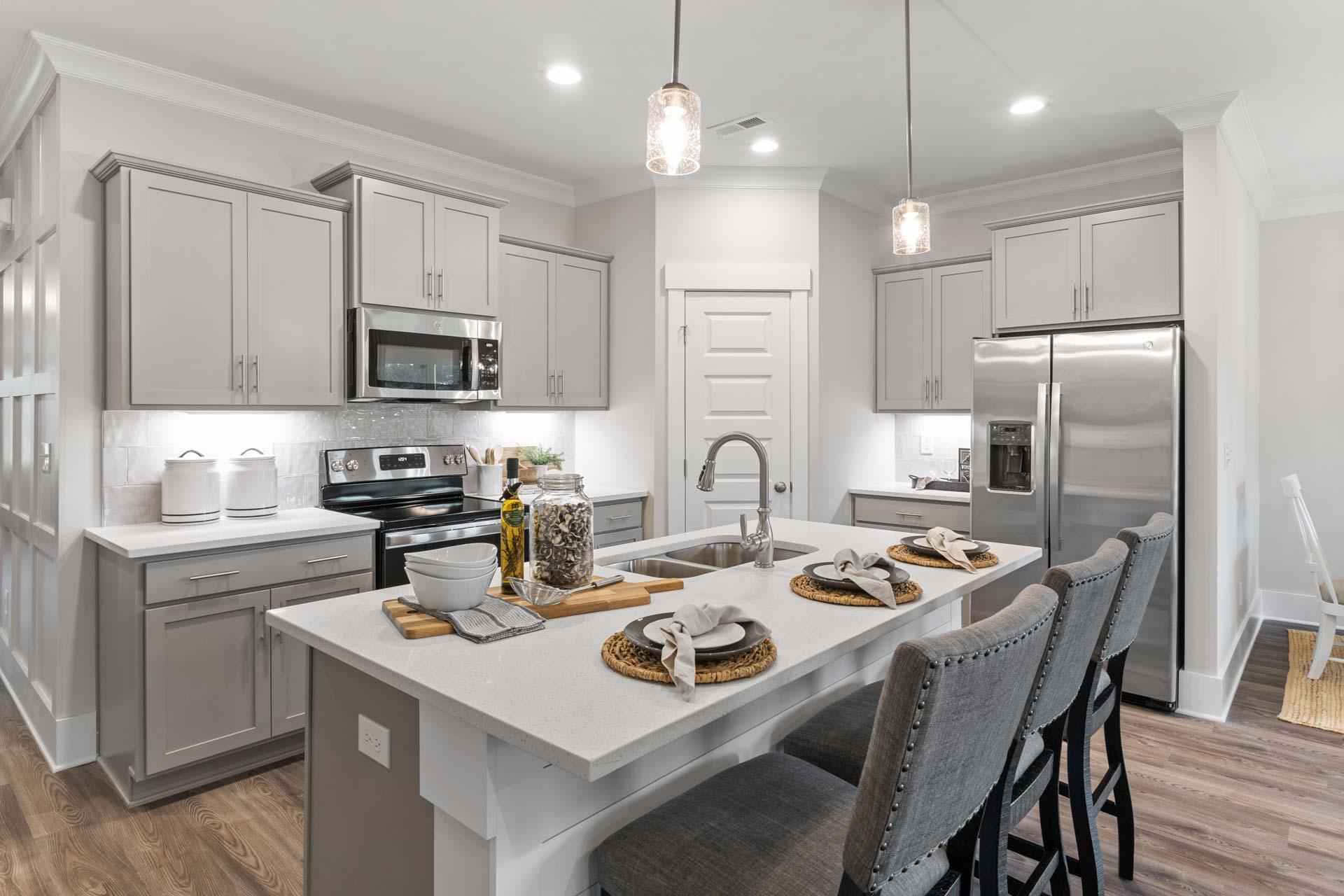 Spacious modern kitchen in The Meadows Athens Alabama with gray shaker cabinets white quartz island stainless steel appliances and pendant lights