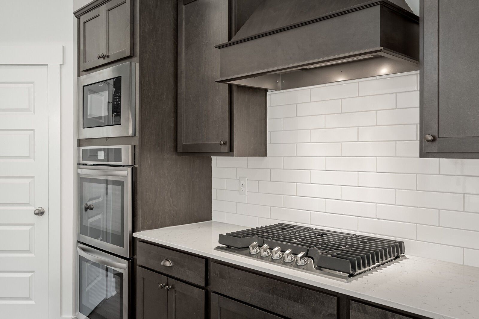 Modern kitchen with dark cabinetry, stainless double oven, and gas cooktop in The Ridgeport C at Woods Crossing, Gallatin.