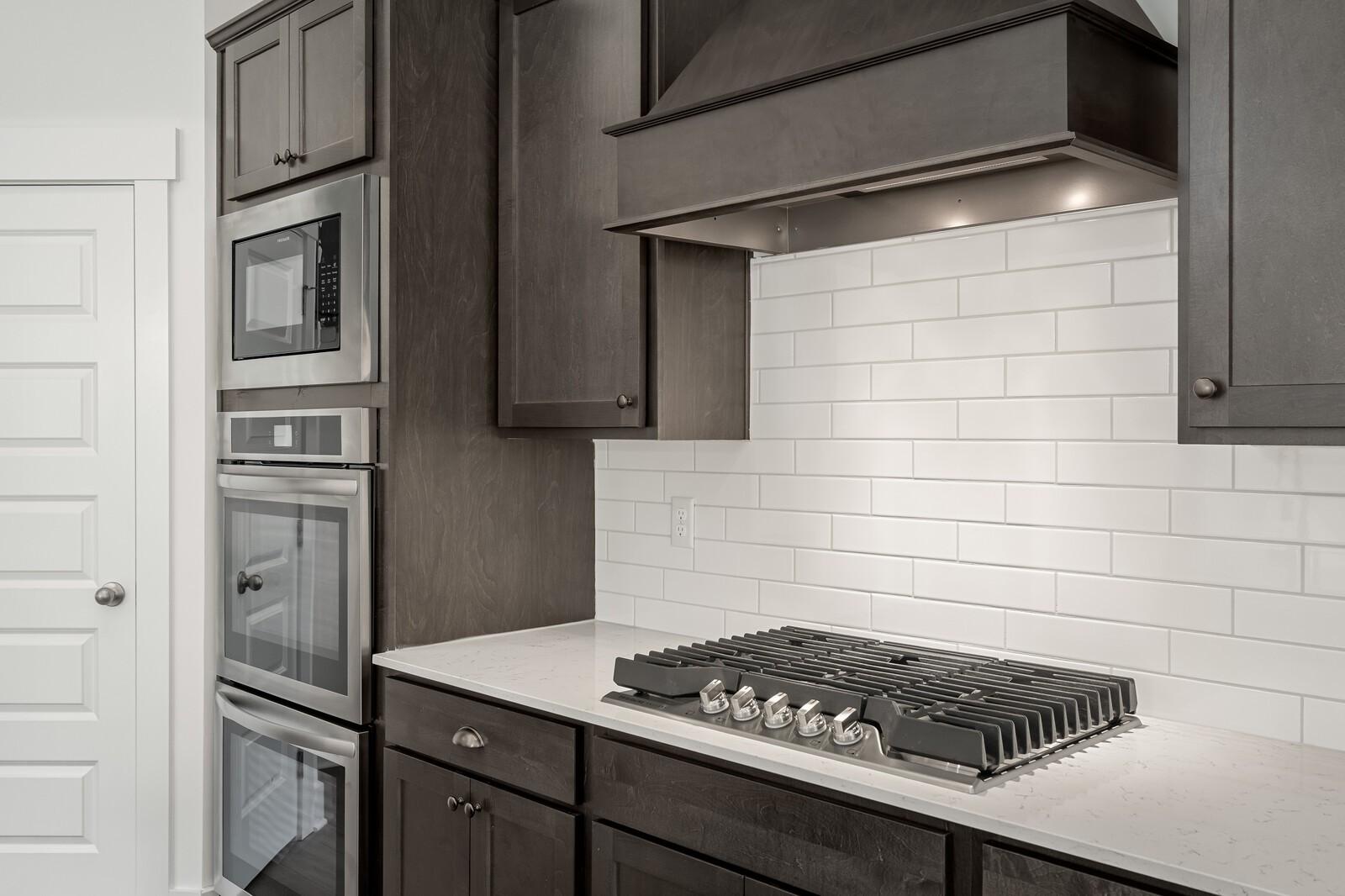 Modern kitchen with dark cabinetry, stainless double oven, and gas cooktop in The Ridgeport C at Woods Crossing, Gallatin.