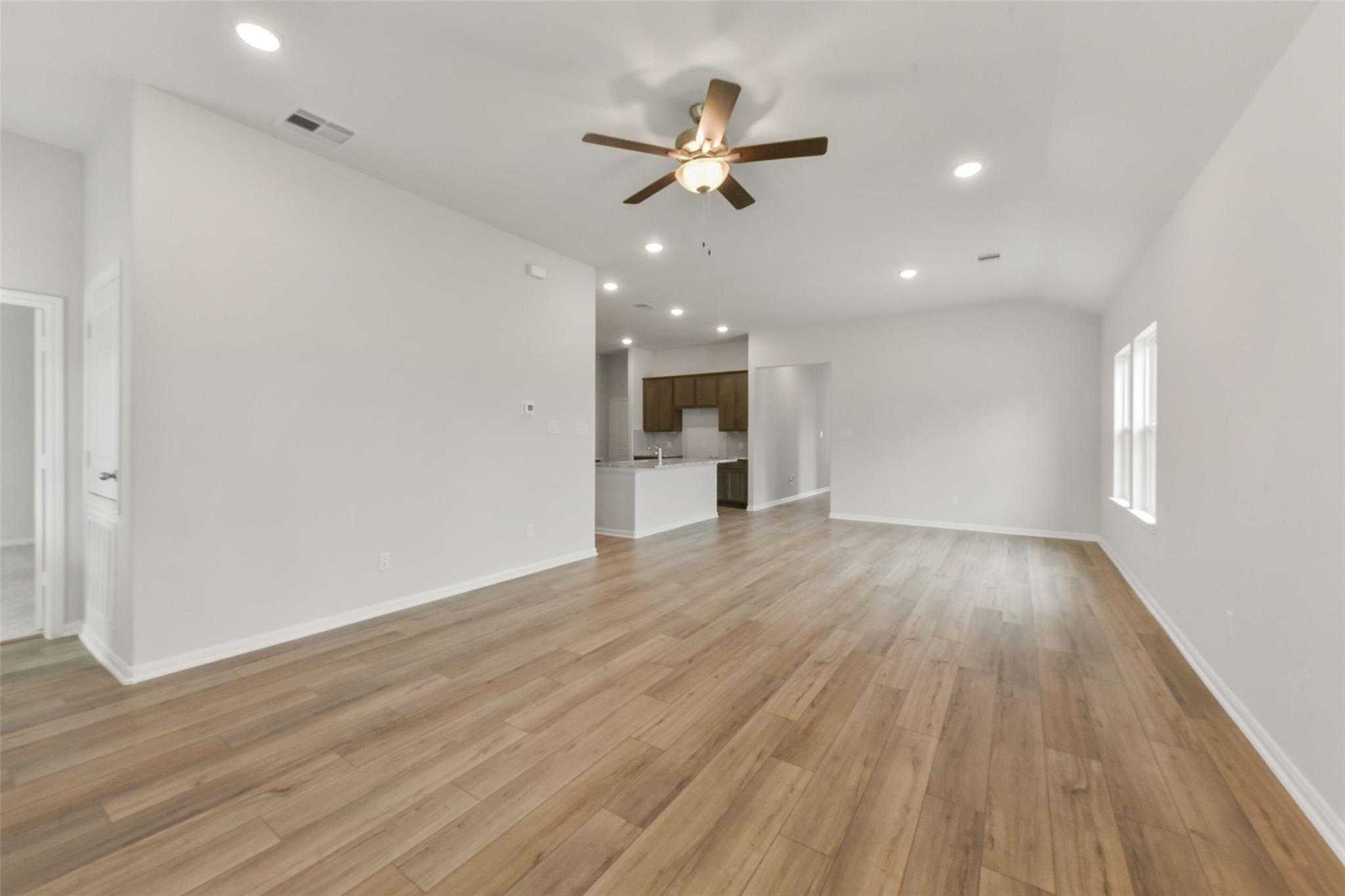 Spacious open living room with hardwood floors, ceiling fan, and adjacent kitchen in Davidson Homes Laguna B, Magnolia, Texas