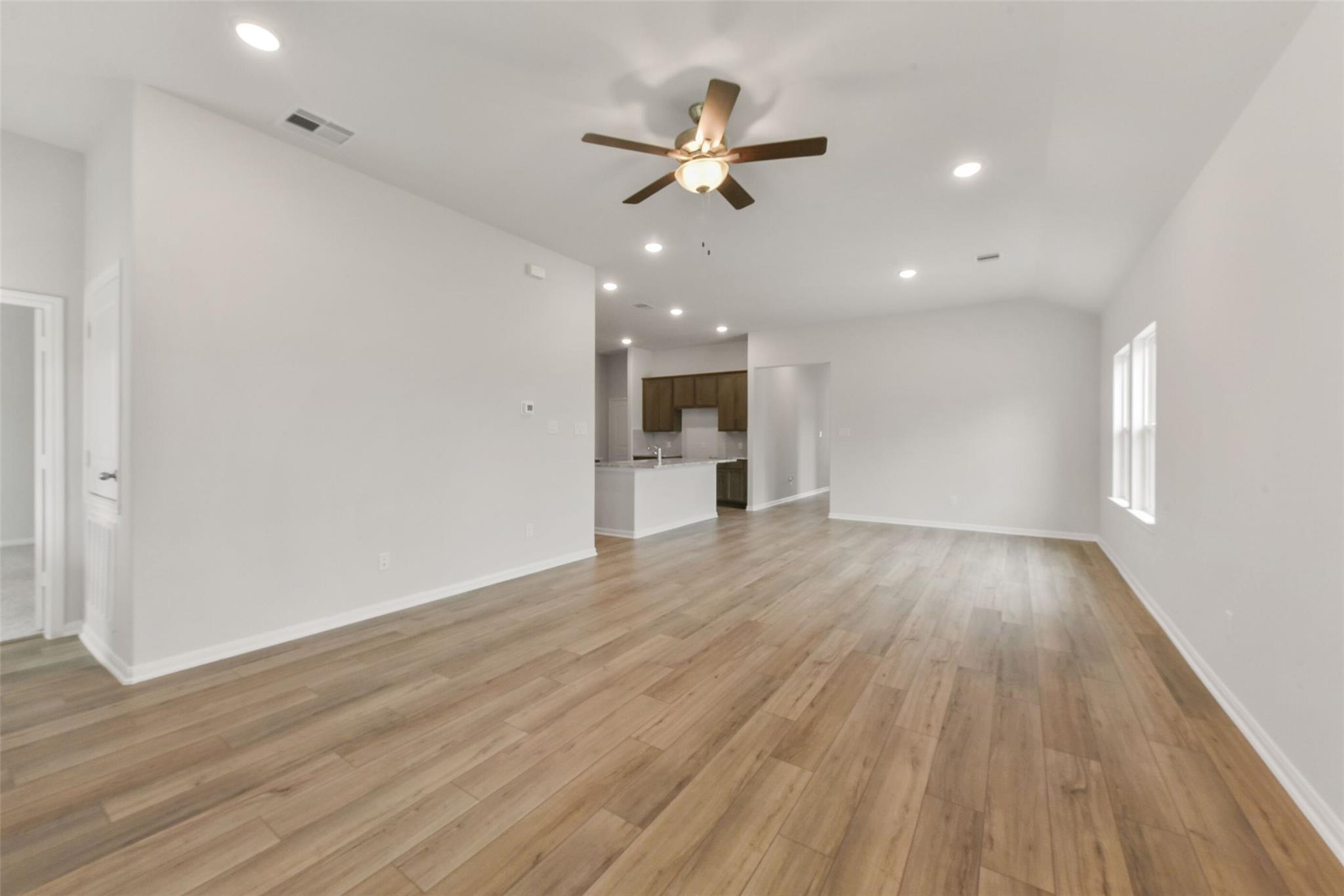 Open living area with hardwood floors, ceiling fan, and adjacent kitchen in Davidson Homes The Laguna B, Magnolia, Texas