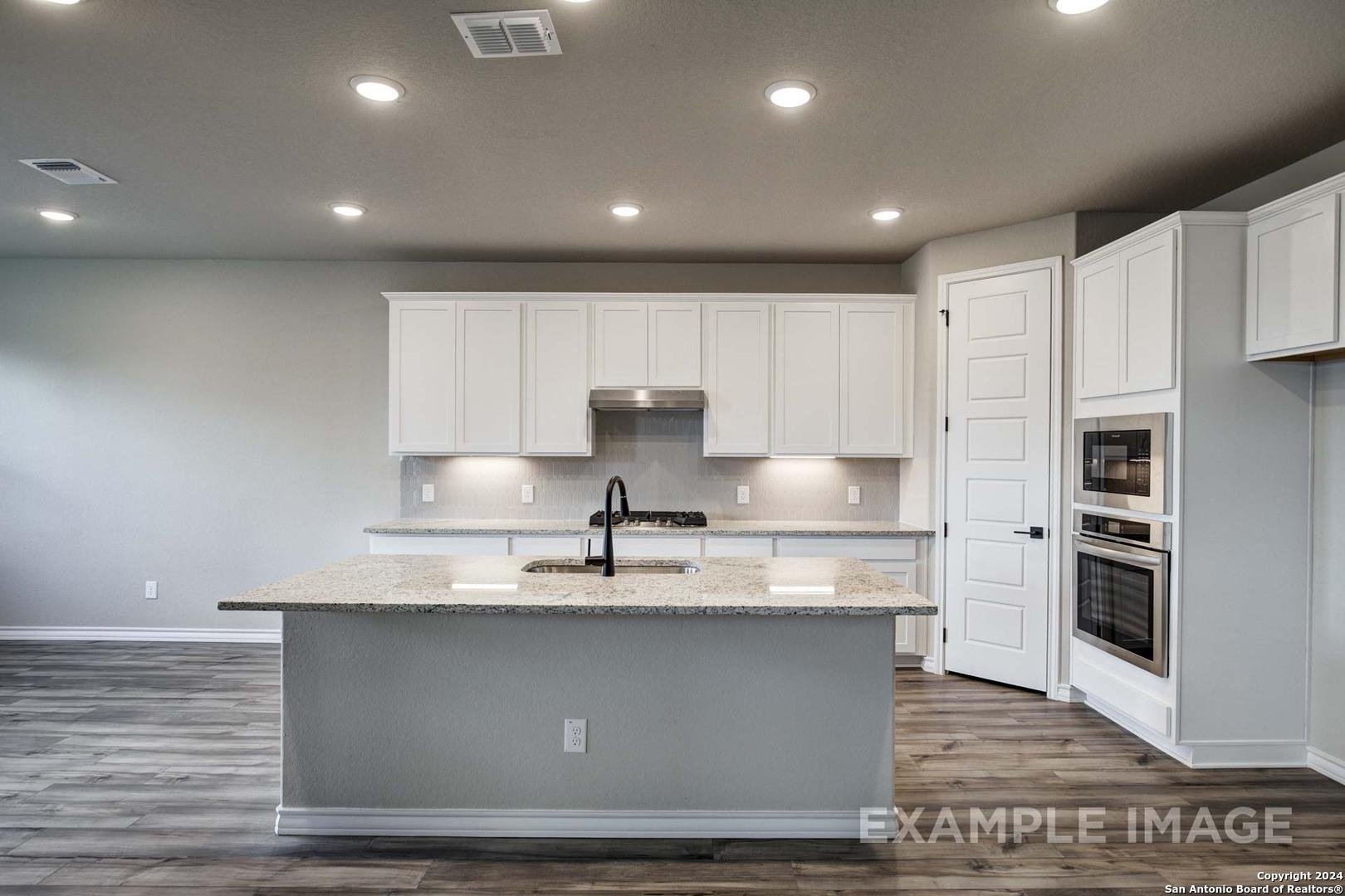 Modern white cabinet kitchen with granite island, stainless double oven, and recessed lighting in Davidson Homes The Rockford G, Ladera San Antonio
