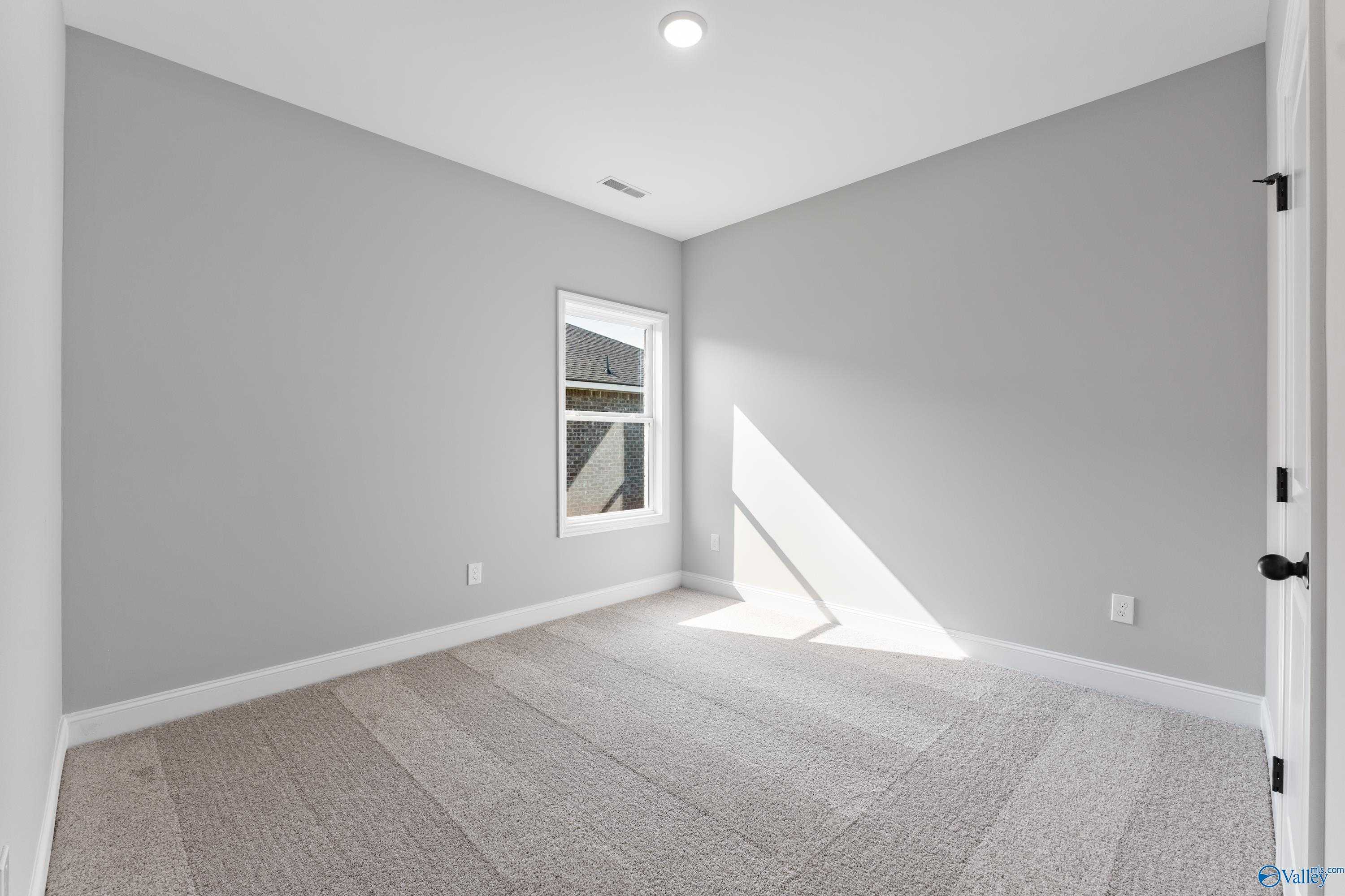 Bright secondary bedroom featuring light gray walls, neutral carpet, and sunlit window in Davidson Homes The Franklin B, Hazel Green, Alabama