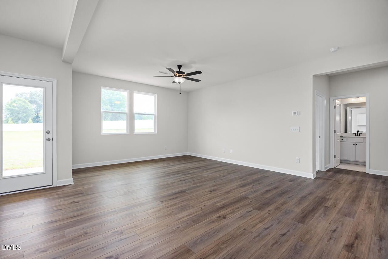 Spacious living area with wood-look flooring, ceiling fan, and backyard access in The Willow B home, Zebulon, NC.