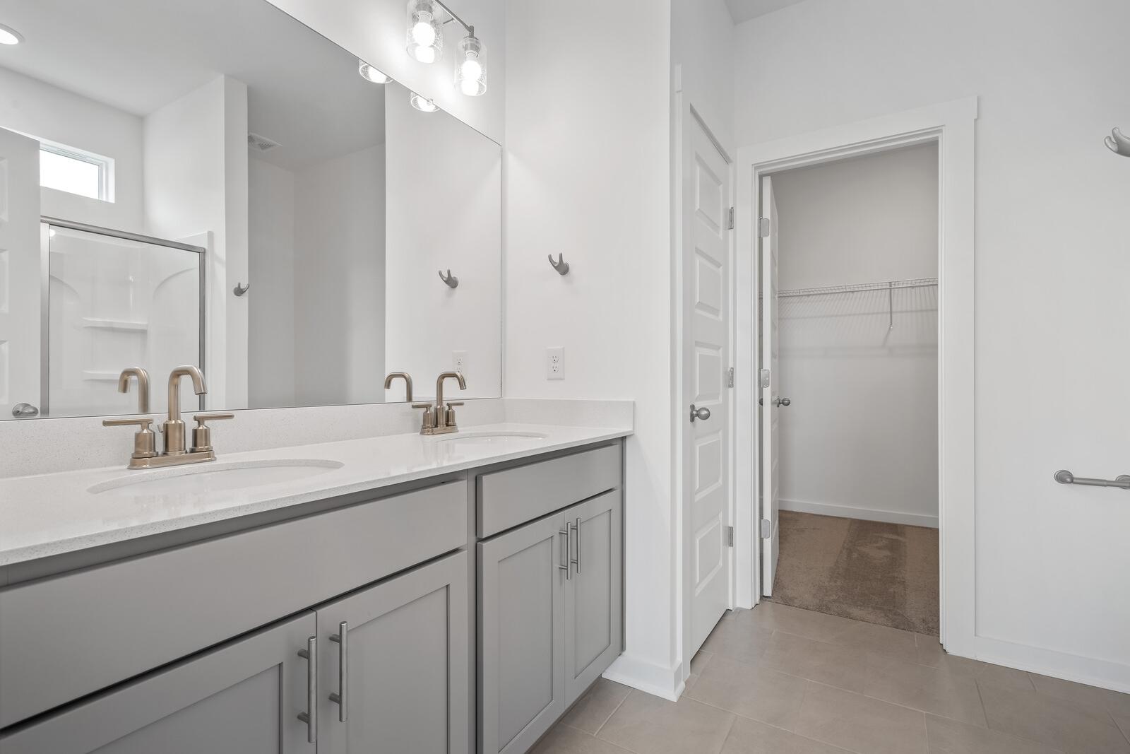Spacious master bathroom in The Asheville with double gray vanity, dual sinks, frameless shower, and open walk-in closet