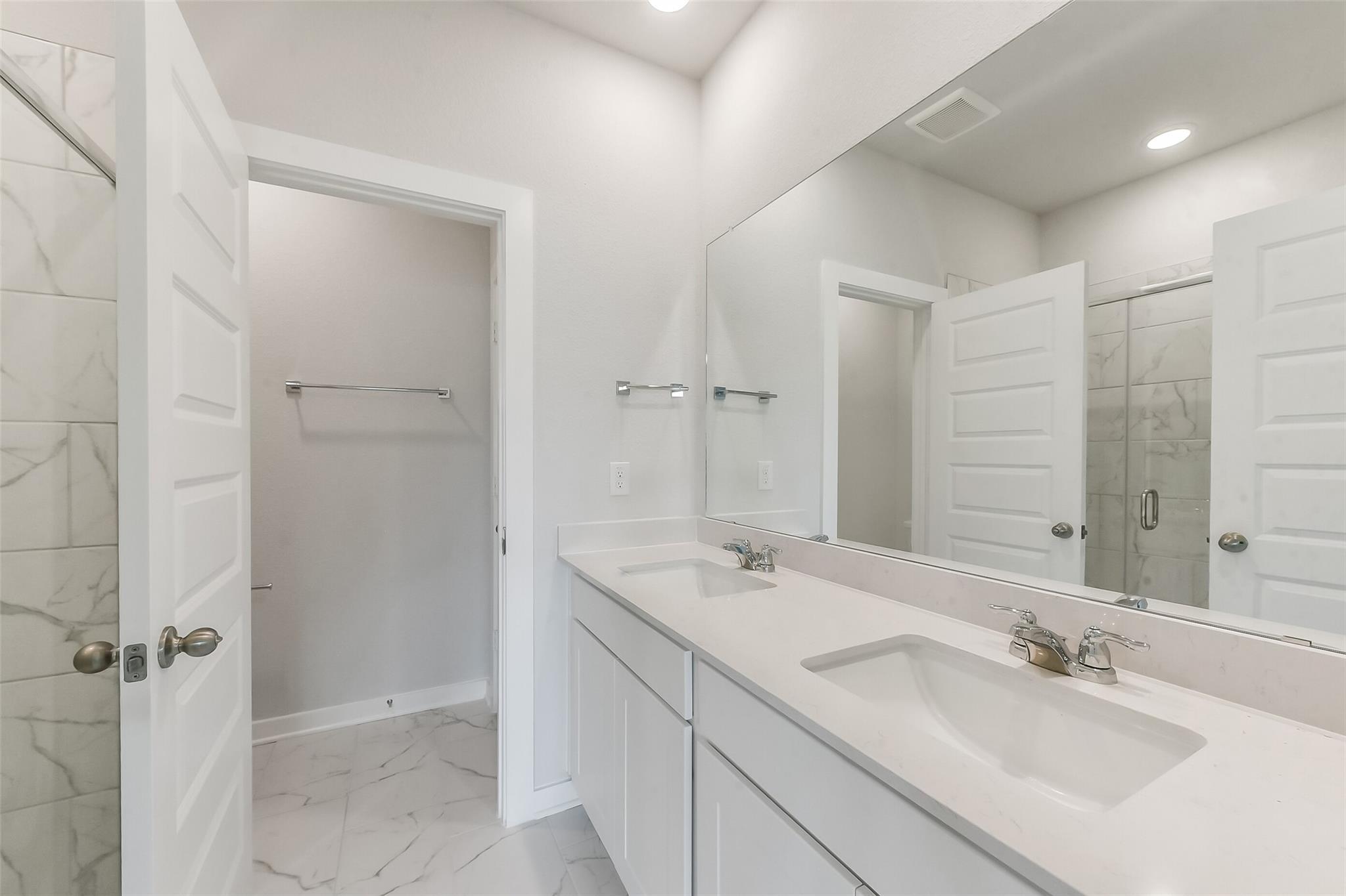 Modern master bathroom double vanity with white quartz counters, marble tile shower and floors in Davidson Homes The Frio G, Magnolia TX