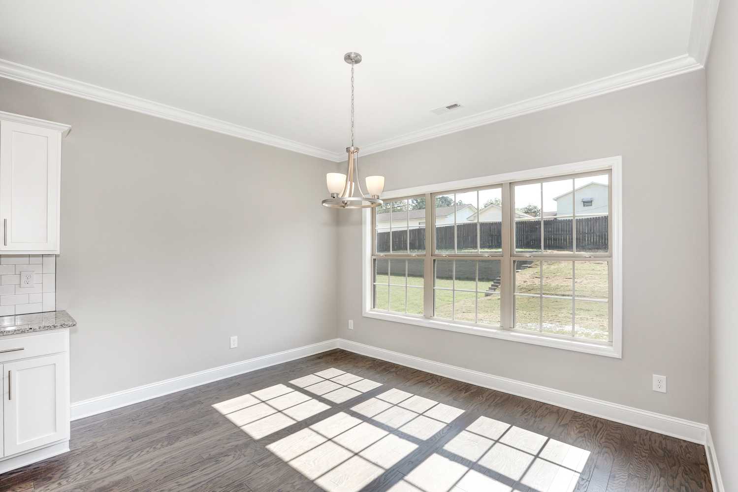 Spacious dining room in The Montgomery home with gray walls, white cabinets, chandelier, large windows, and hardwood floors