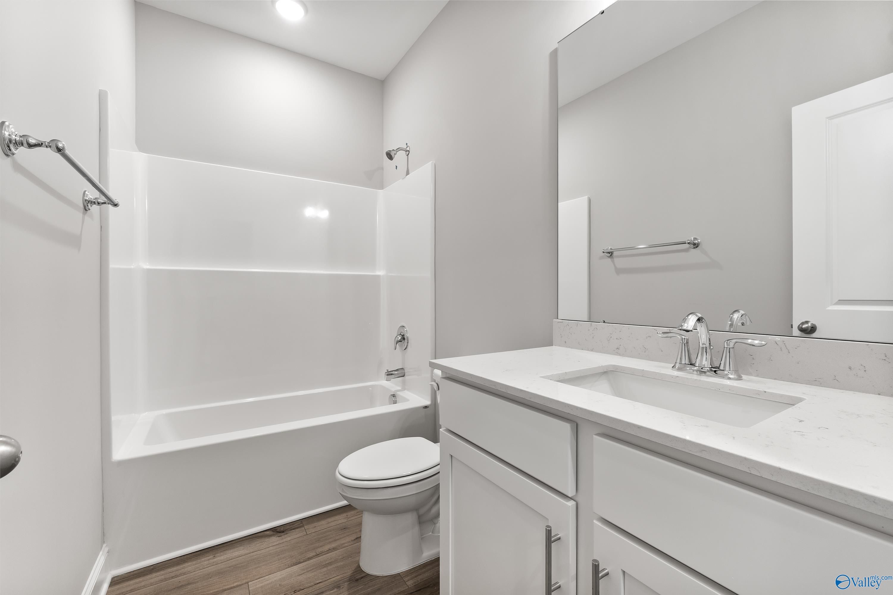 Modern bathroom with white tub-shower combo, quartz vanity, toilet, and wood floors in Davidson Homes The Franklin C, Huntsville, AL