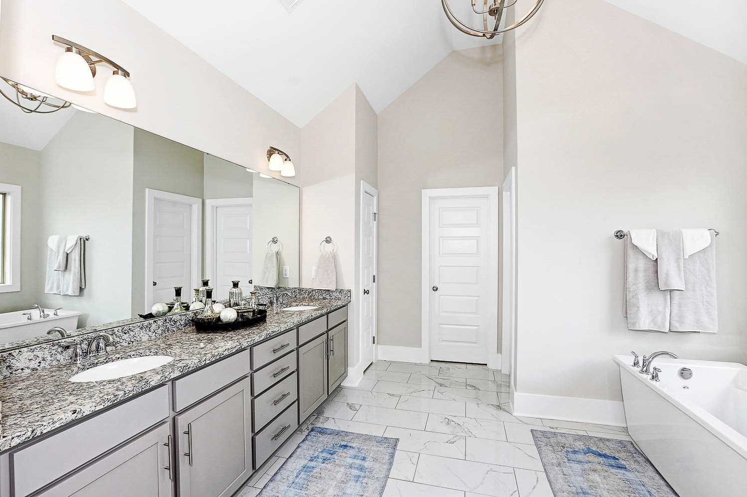Spacious master bathroom in The Finleigh featuring double granite vanity, freestanding tub, and vaulted ceiling