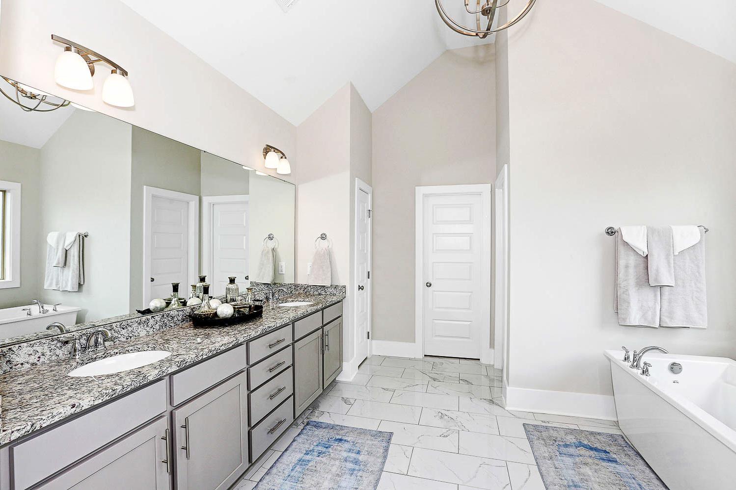 Spacious master bathroom in The Finleigh featuring double vanity, freestanding tub, granite counters, and soft lighting