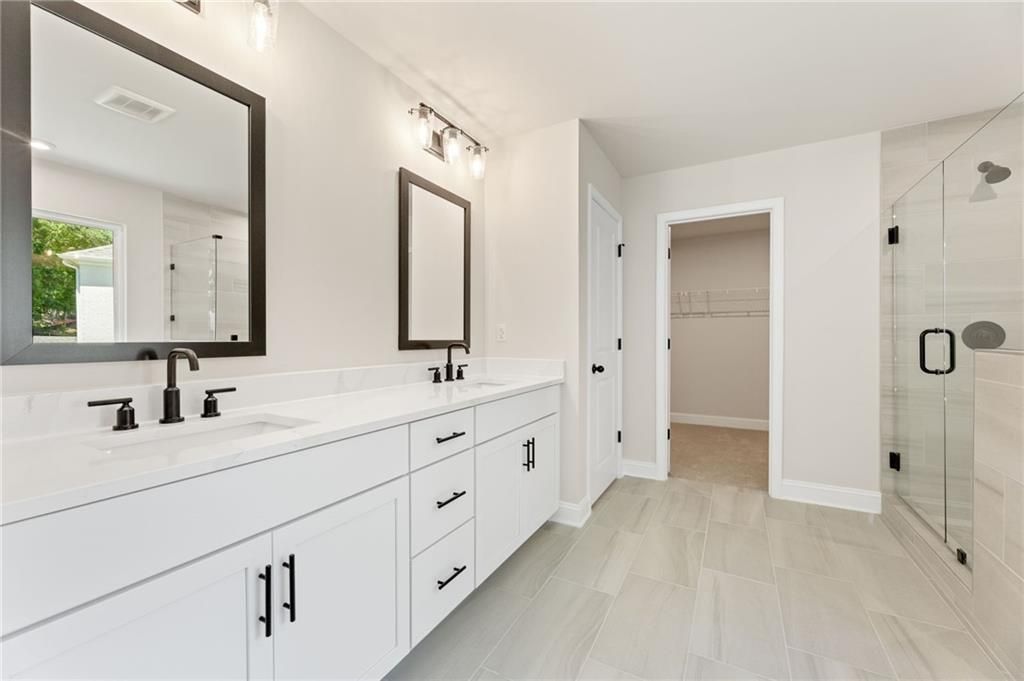 Modern master bathroom with double white vanity, black faucets, frameless glass shower in Davidson Homes The Hickory E, Buford, Georgia