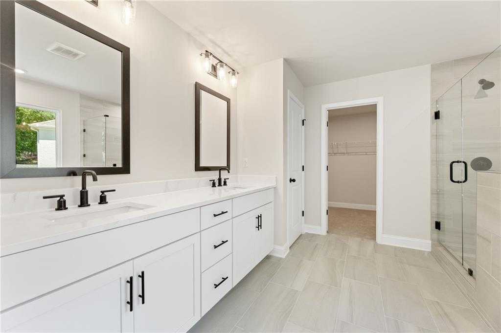 Elegant master bathroom featuring double white vanity, frameless glass shower, and walk-in closet in Davidson Homes The Hickory E, Buford, GA