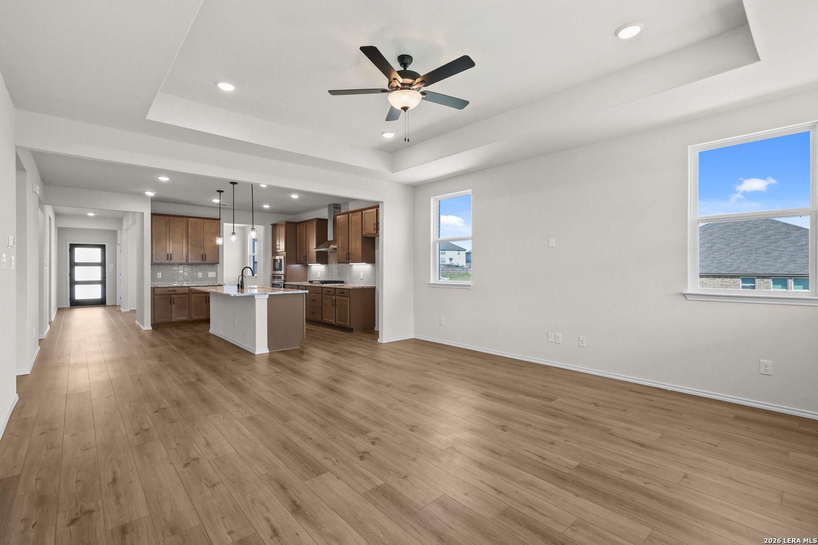 Open-concept living area with wood-look flooring, tray ceiling, and kitchen island in Davidson Homes Glenwood E, San Antonio TX