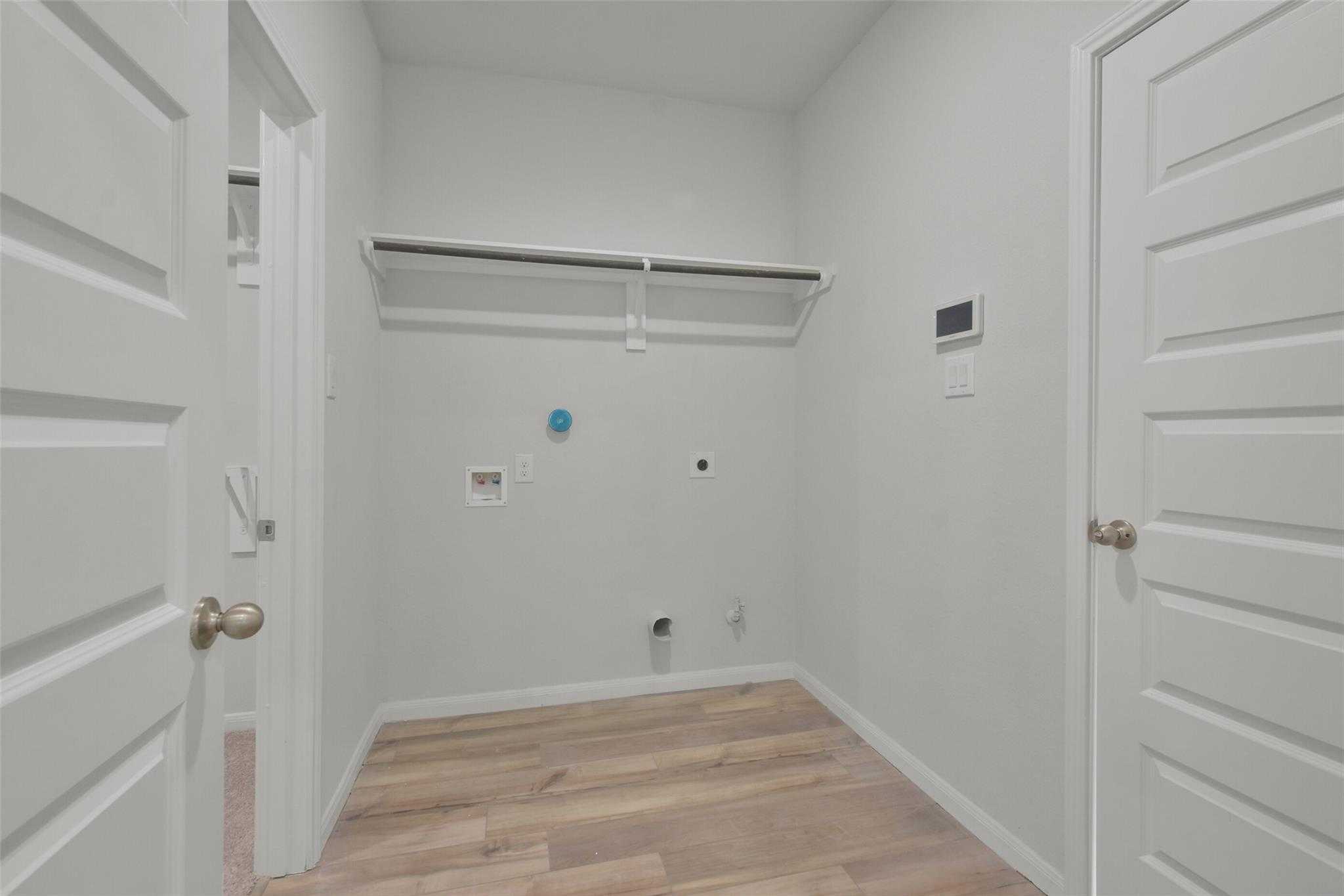 Bright laundry room with open shelving, washer-dryer hookups, and wood flooring in Davidson Homes The Tierra A, Dayton, Texas
