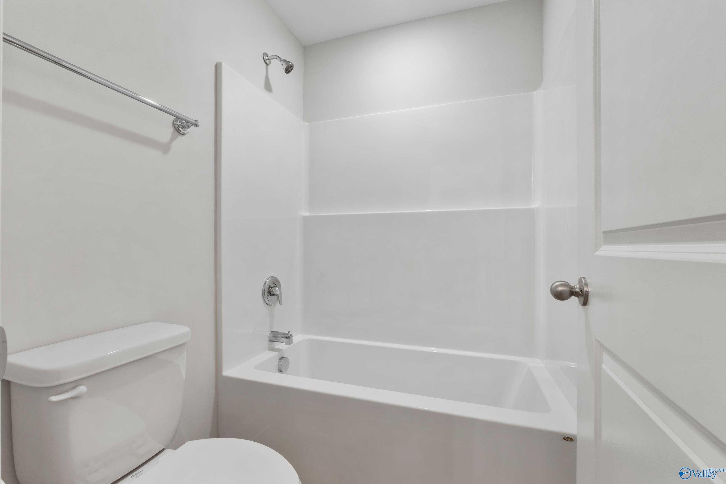 Bright white bathroom with tub-shower combo, modern toilet, and towel bar in Davidson Homes The Chelsea C, Harvest, Alabama