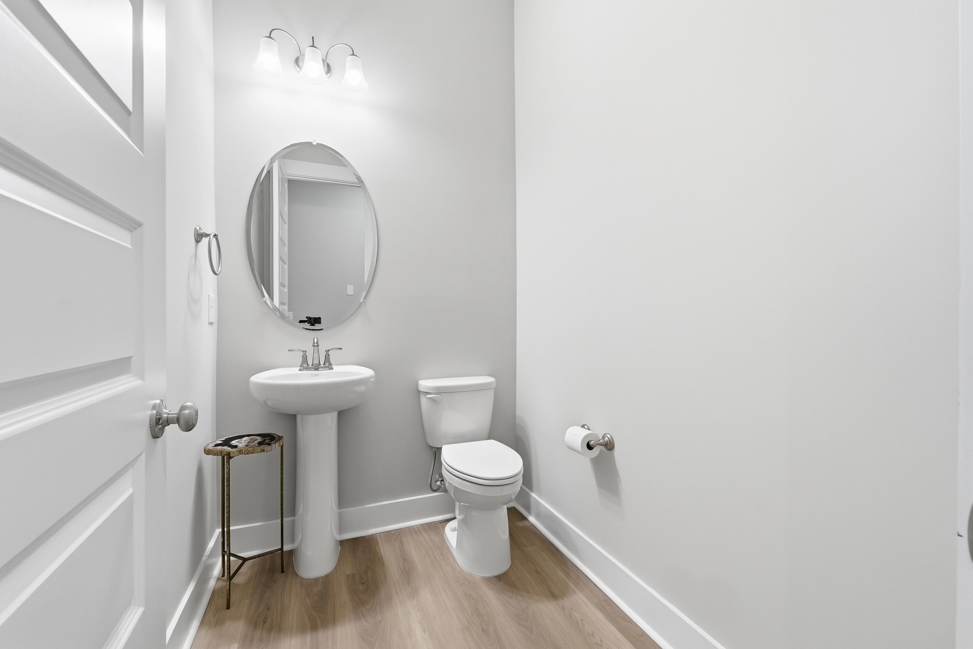 Elegant powder room at The Meadows at Hampton Cove in Owens Cross Roads Alabama with pedestal sink oval mirror and hardwood floors