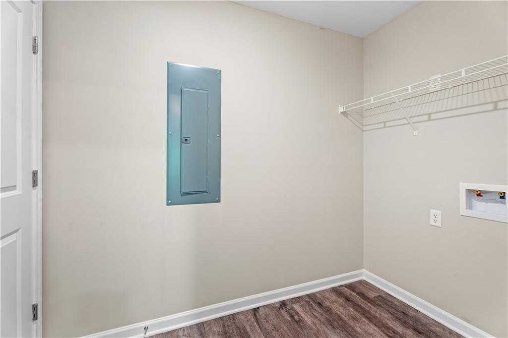 Modern laundry room with utility sink, electrical panel, wire shelving, and hardwood floors in Davidson Homes The Washington, Phenix City