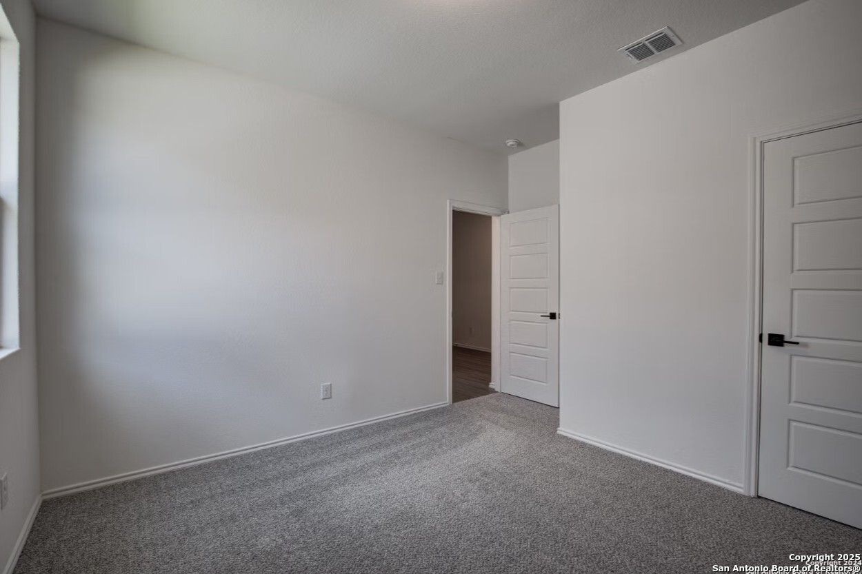 Spacious secondary bedroom with white walls, gray carpet, double doors, and window in Davidson Homes The Daphne H, Seguin, Texas