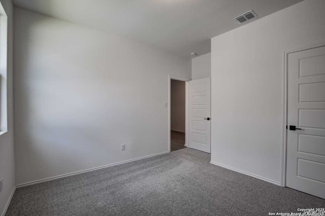 Spacious secondary bedroom with white walls, gray carpet, double doors, and window in Davidson Homes The Daphne H, Seguin, Texas