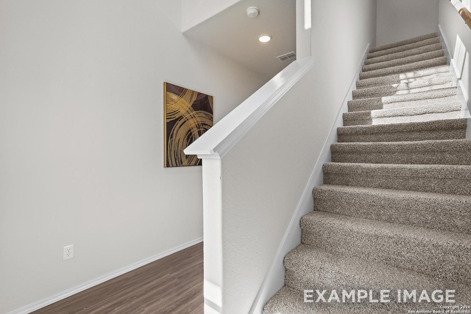 Elegant beige carpeted staircase with white railing and abstract wall art in 2-story Trinity B home, Davidson Homes, San Antonio