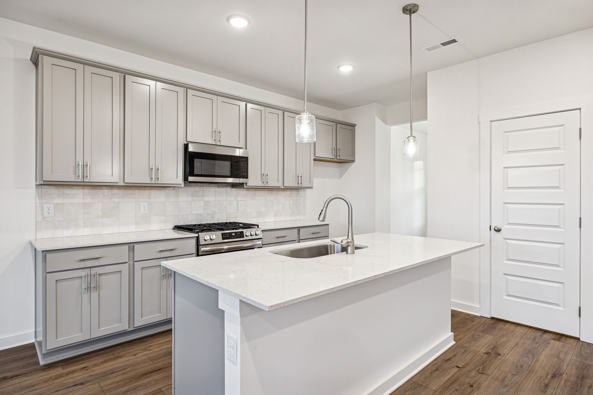 Modern kitchen featuring gray shaker cabinets, white quartz island, stainless steel appliances in Davidson Homes The Willow, Calista Farms, TN
