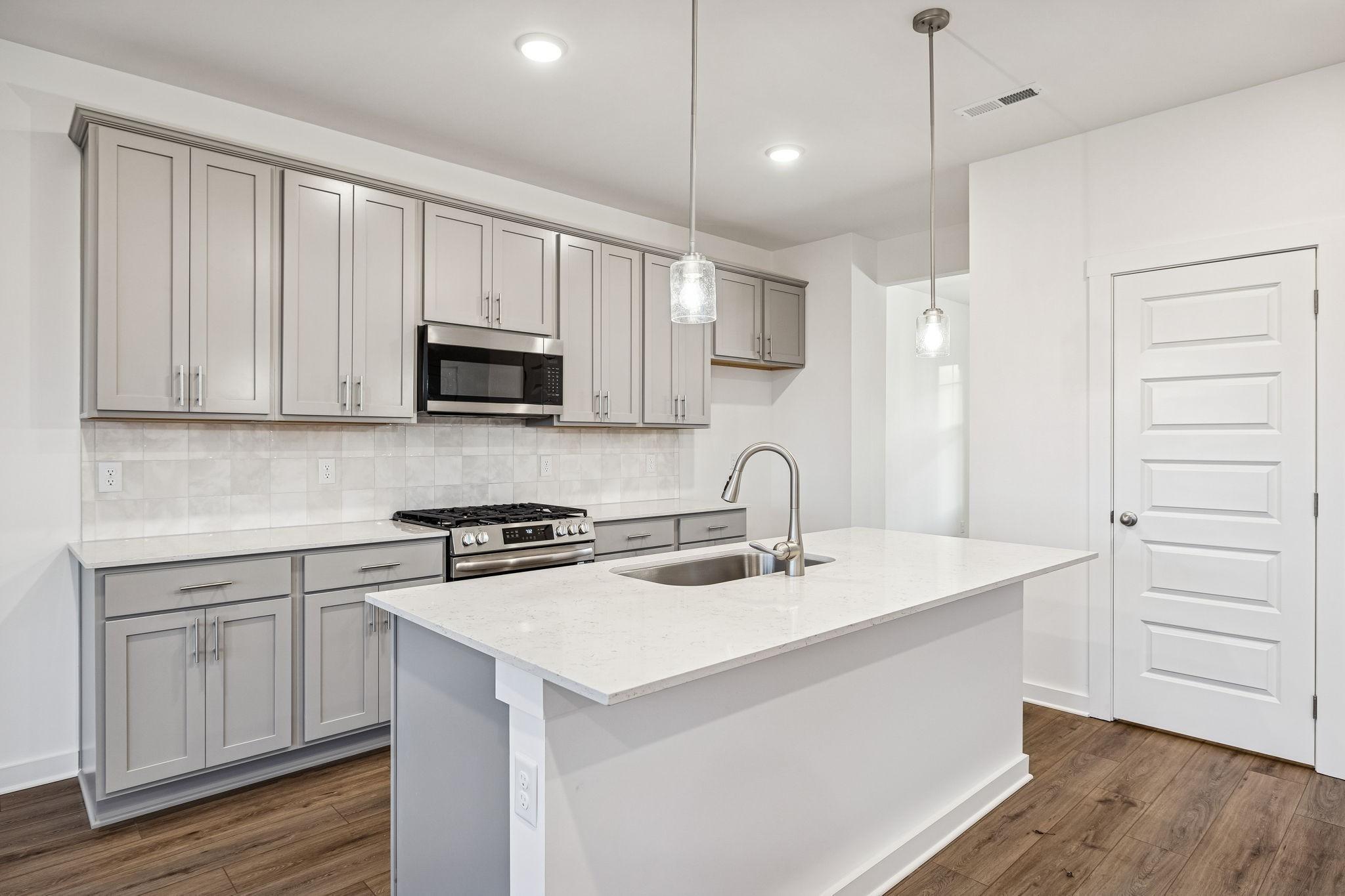 Modern kitchen featuring gray shaker cabinets, white quartz island, stainless steel appliances in Davidson Homes The Willow, Calista Farms, TN