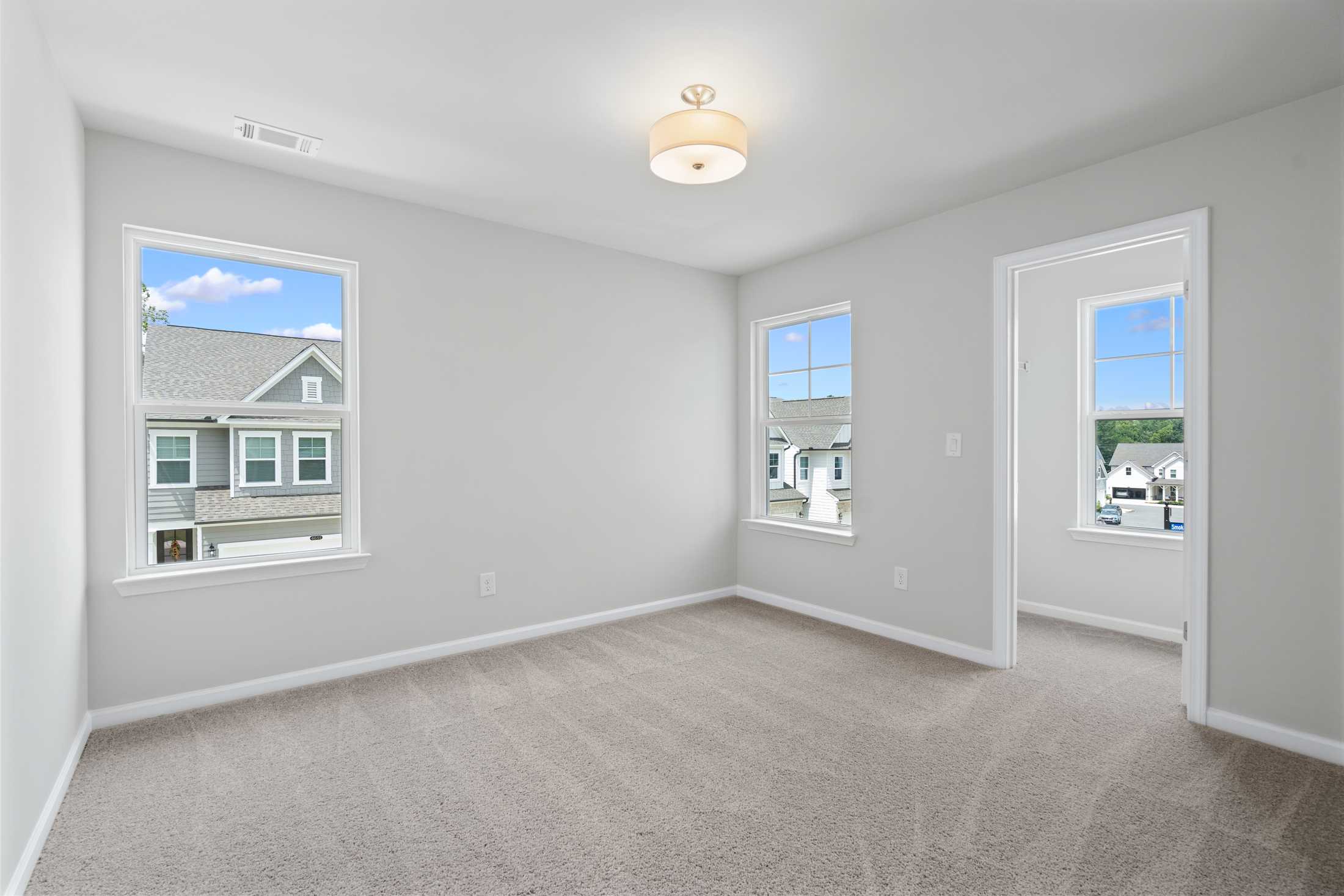 Bright secondary bedroom in The Cary A with light gray walls, beige carpet, large windows overlooking suburban homes