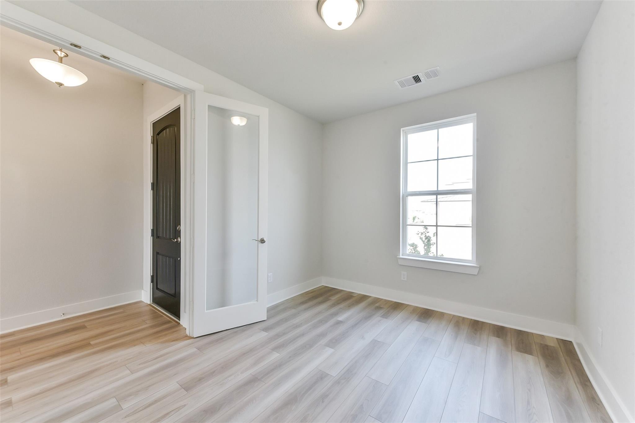 Bright secondary bedroom with luxury vinyl plank flooring, frosted glass door, and natural light in Davidson Homes The Edward A, Lago Mar